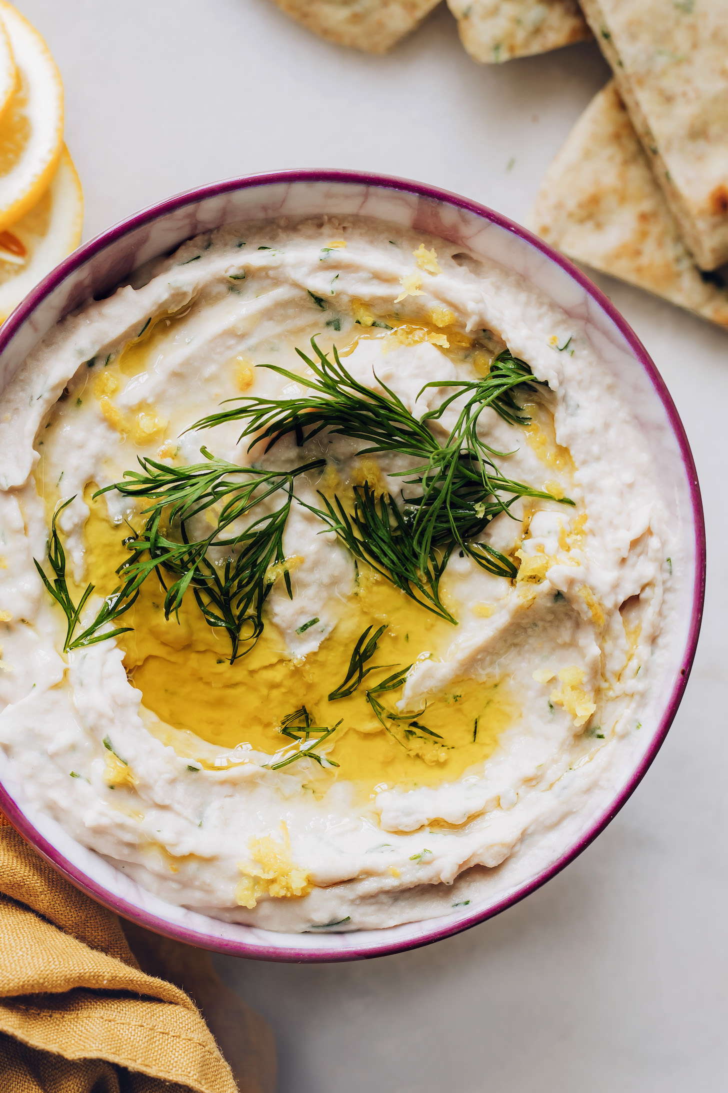 Bowl of white bean hummus topped with fresh dill and olive oil