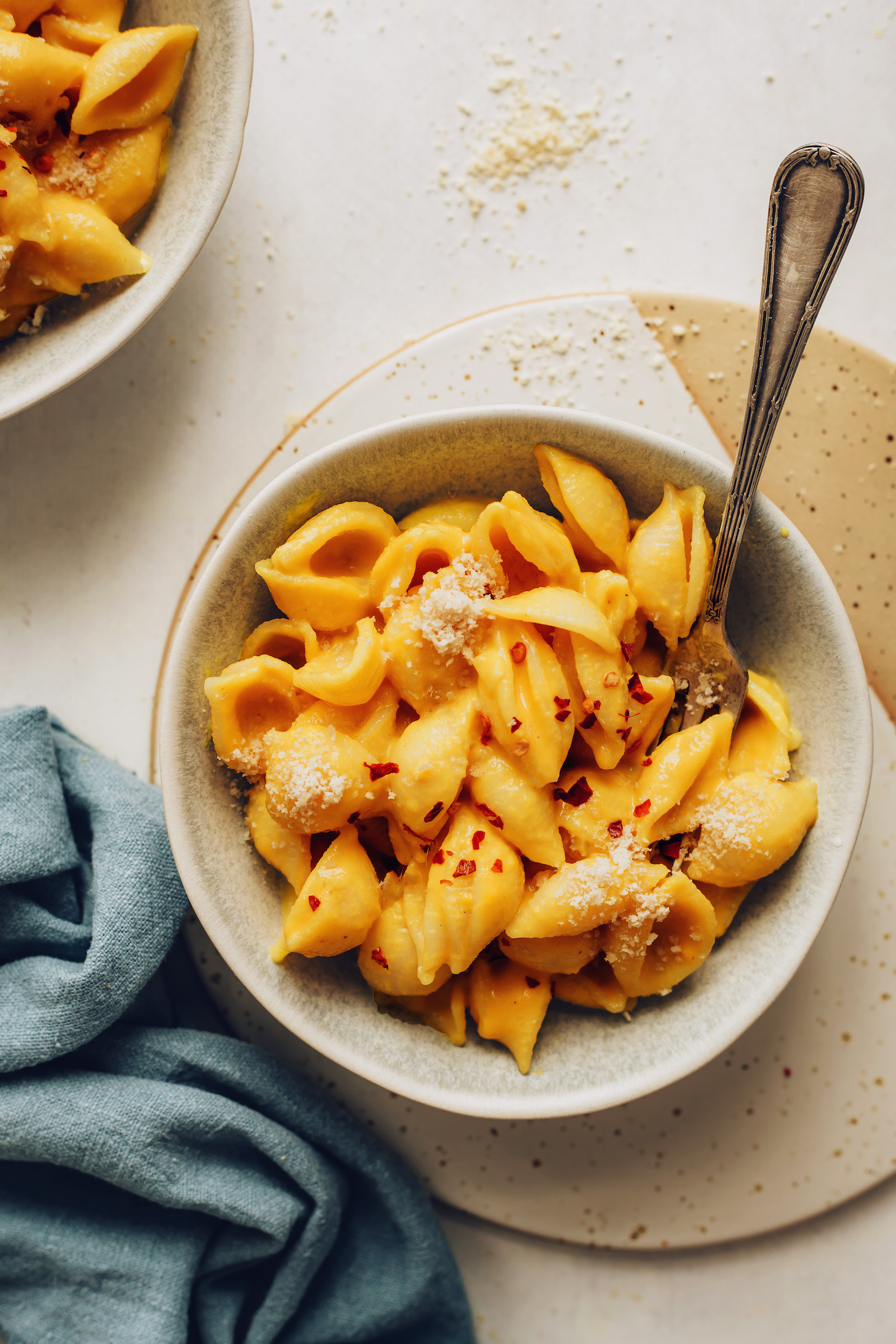 Bowl of vegan mac and cheese topped with red pepper flakes and vegan parmesan