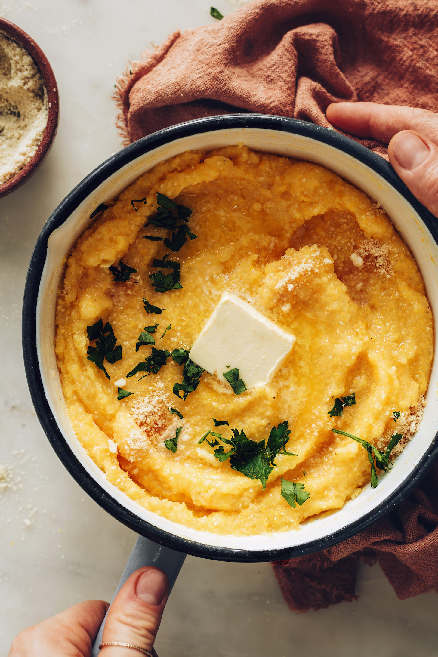 Pan of vegan polenta topped with vegan butter, parsley, and vegan parmesan