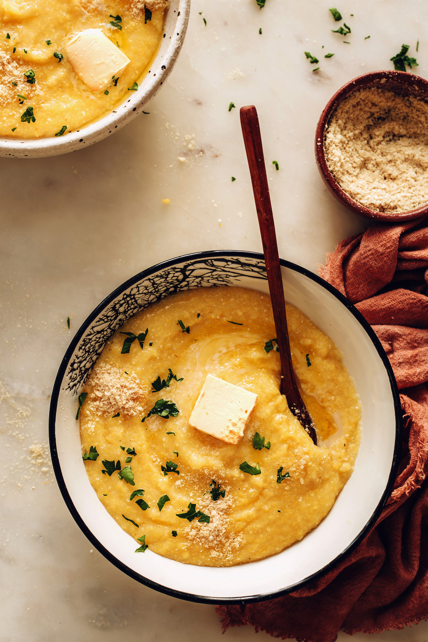 Bowls of vegan polenta next to a small bowl of vegan parmesan