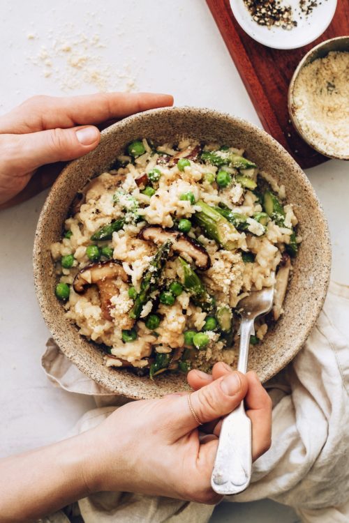 Holding a fork in a bowl of vegan risotto with spring vegetables