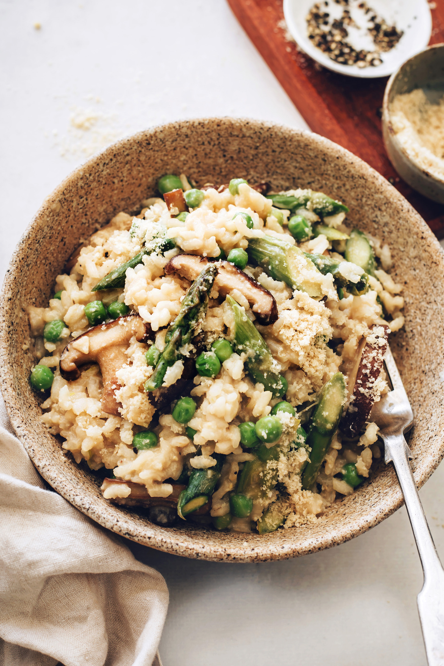 Black pepper and vegan parmesan in small bowls next to a large bowl of vegan risotto