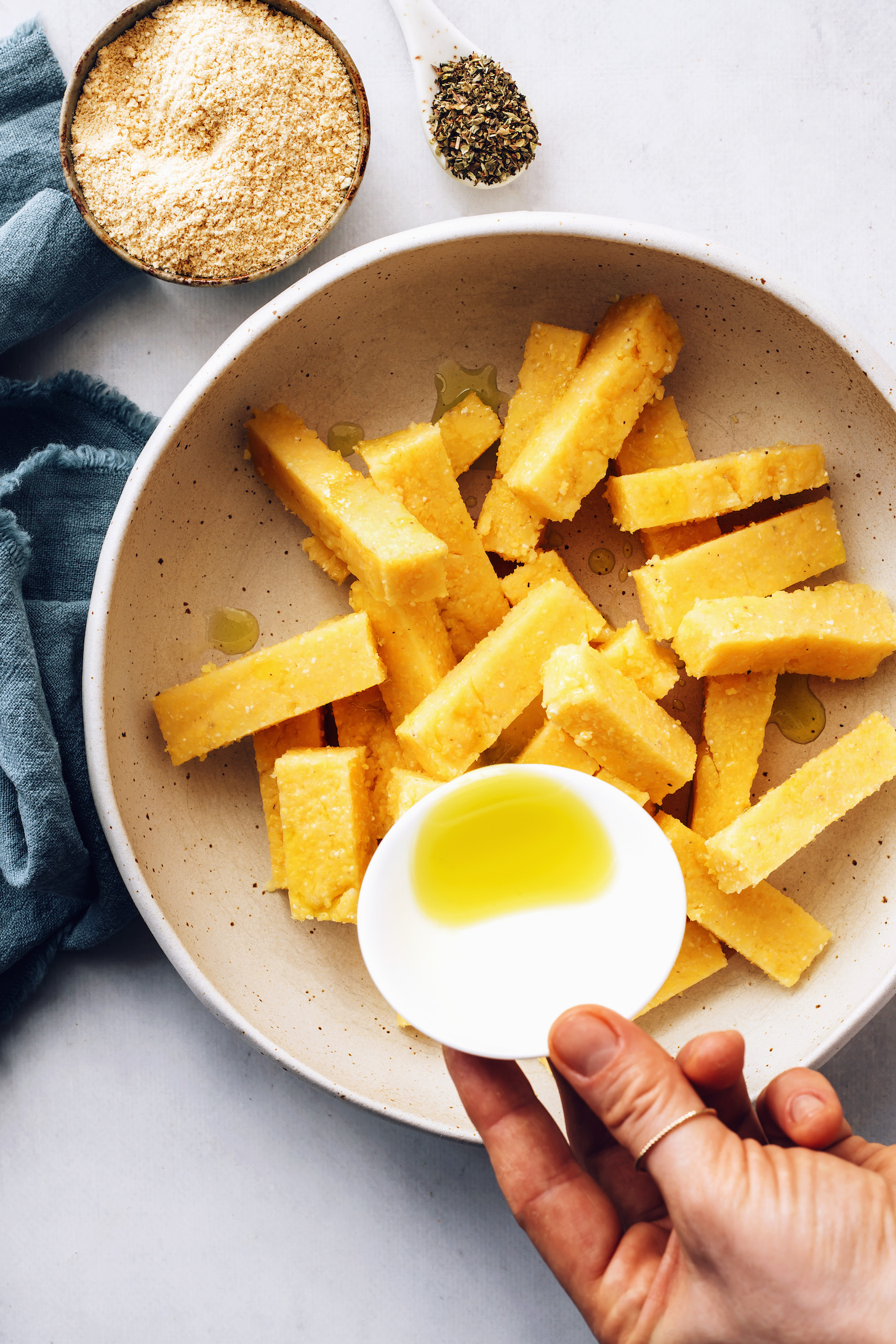 Pouring olive oil over pieces of sliced polenta for making polenta fries