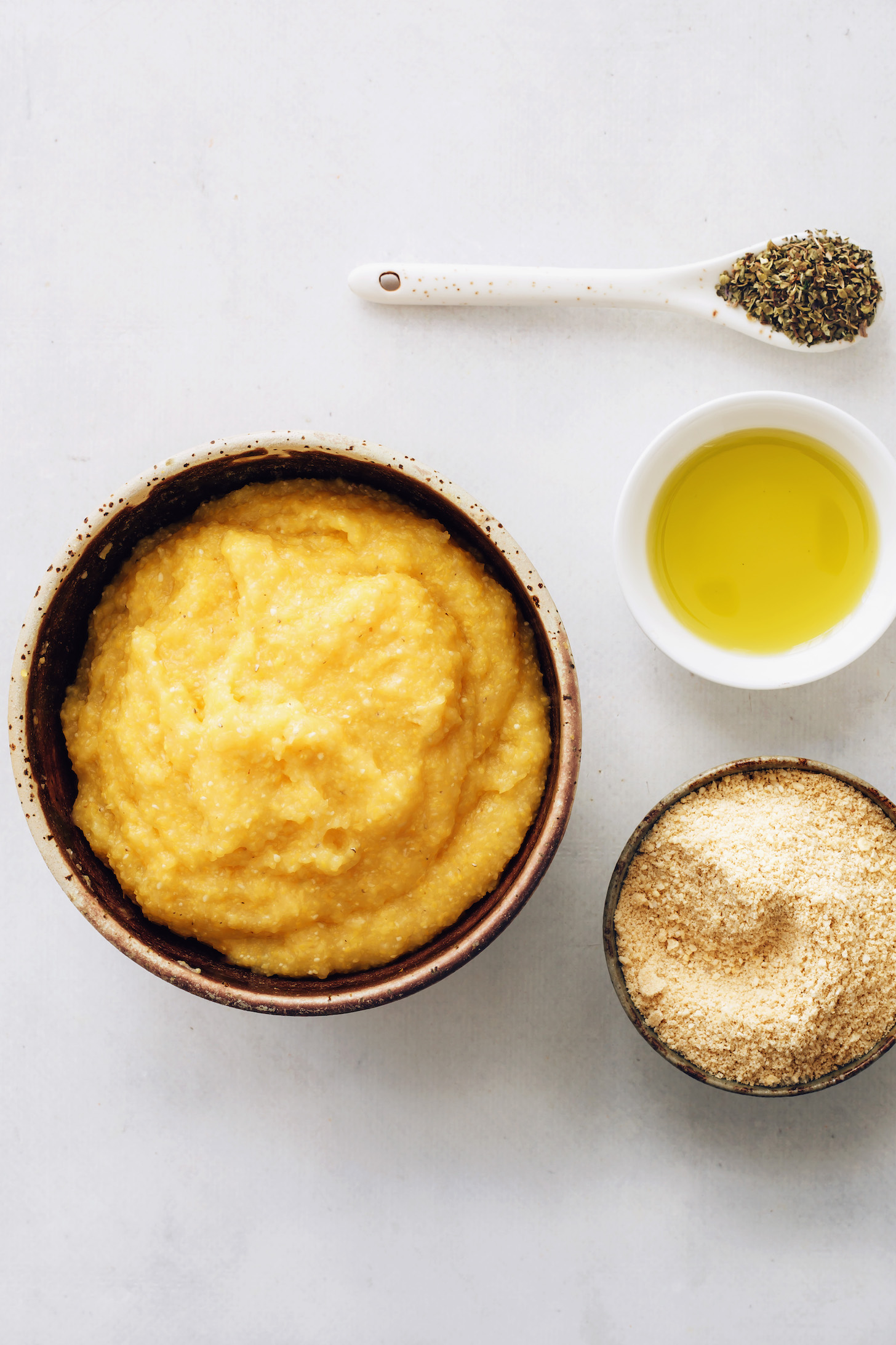 Bowls of homemade polenta, Italian herbs, olive oil, and vegan parmesan cheese