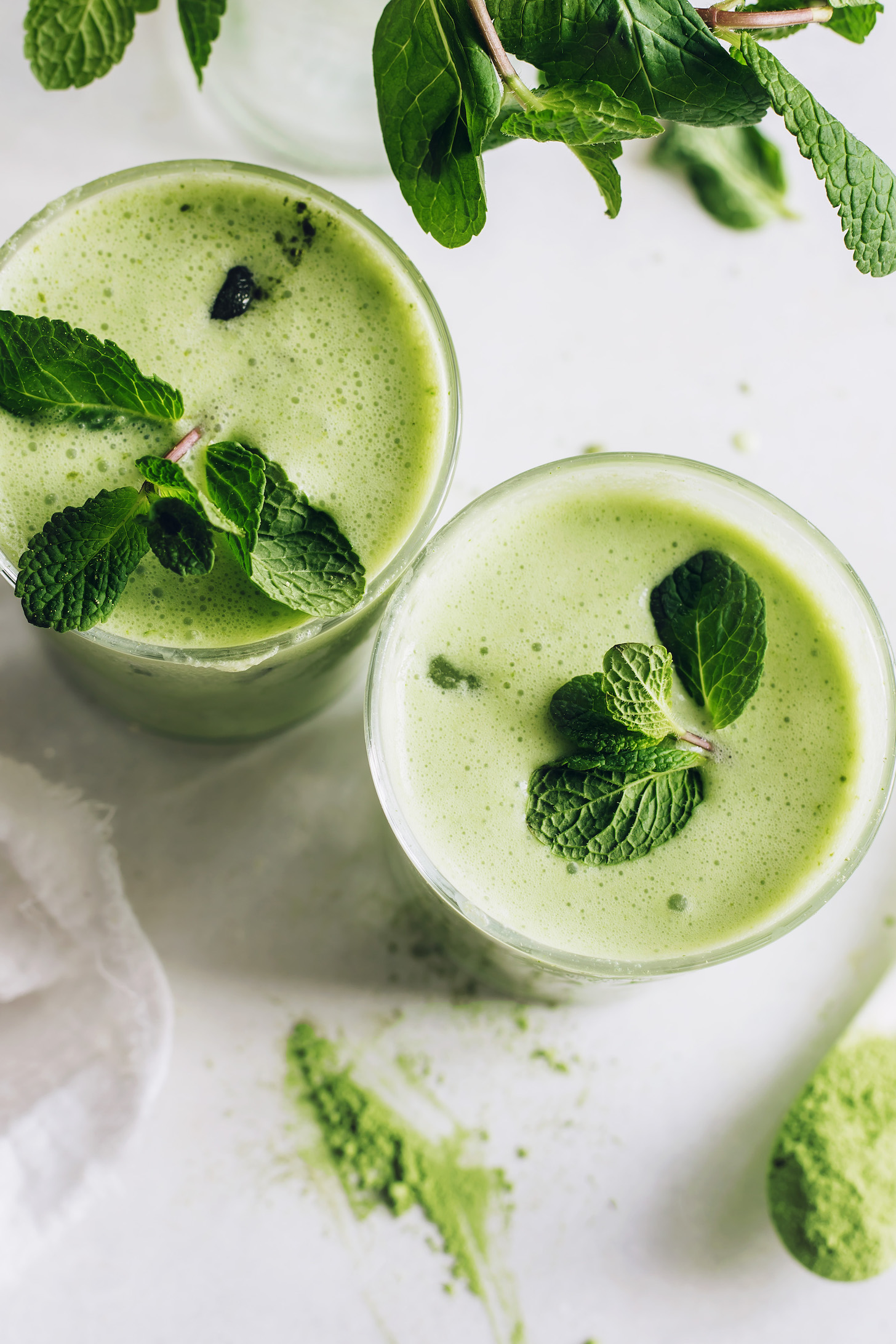 Top down shot of two glasses of frothy iced matcha lattes with fresh mint