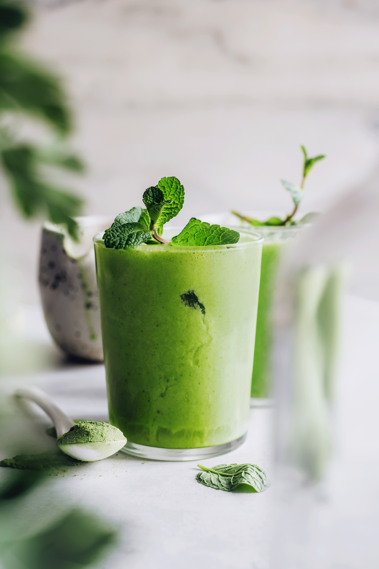 Spoonful of matcha powder next to glasses of mint matcha lattes