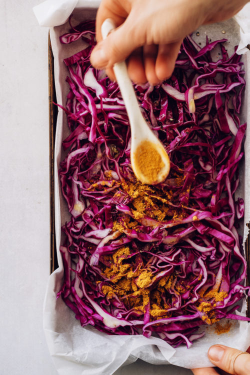 Sprinkling curry powder over a pan of thinly sliced cabbage