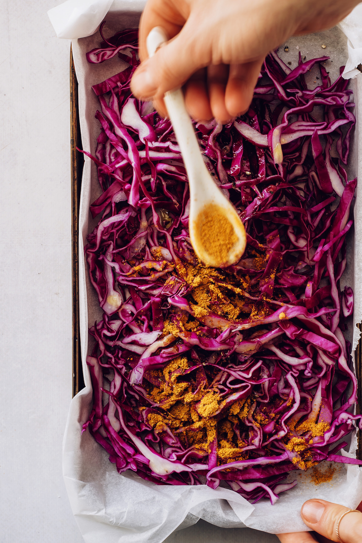 Using a spoon to sprinkle curry powder on thinly sliced red cabbage