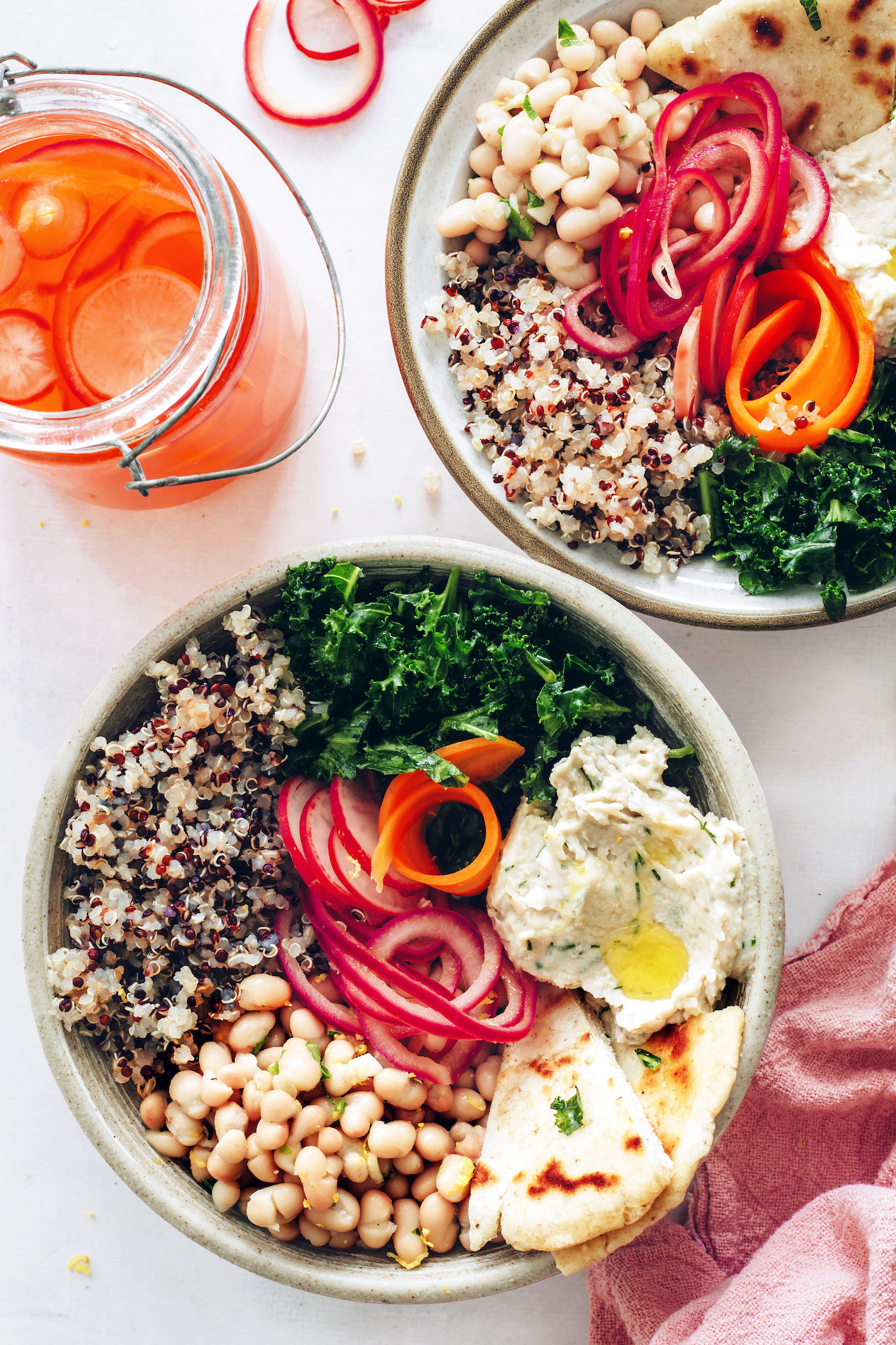 Two spring Buddha bowls with kale, hummus, quinoa, pickled veggies, and marinated white beans