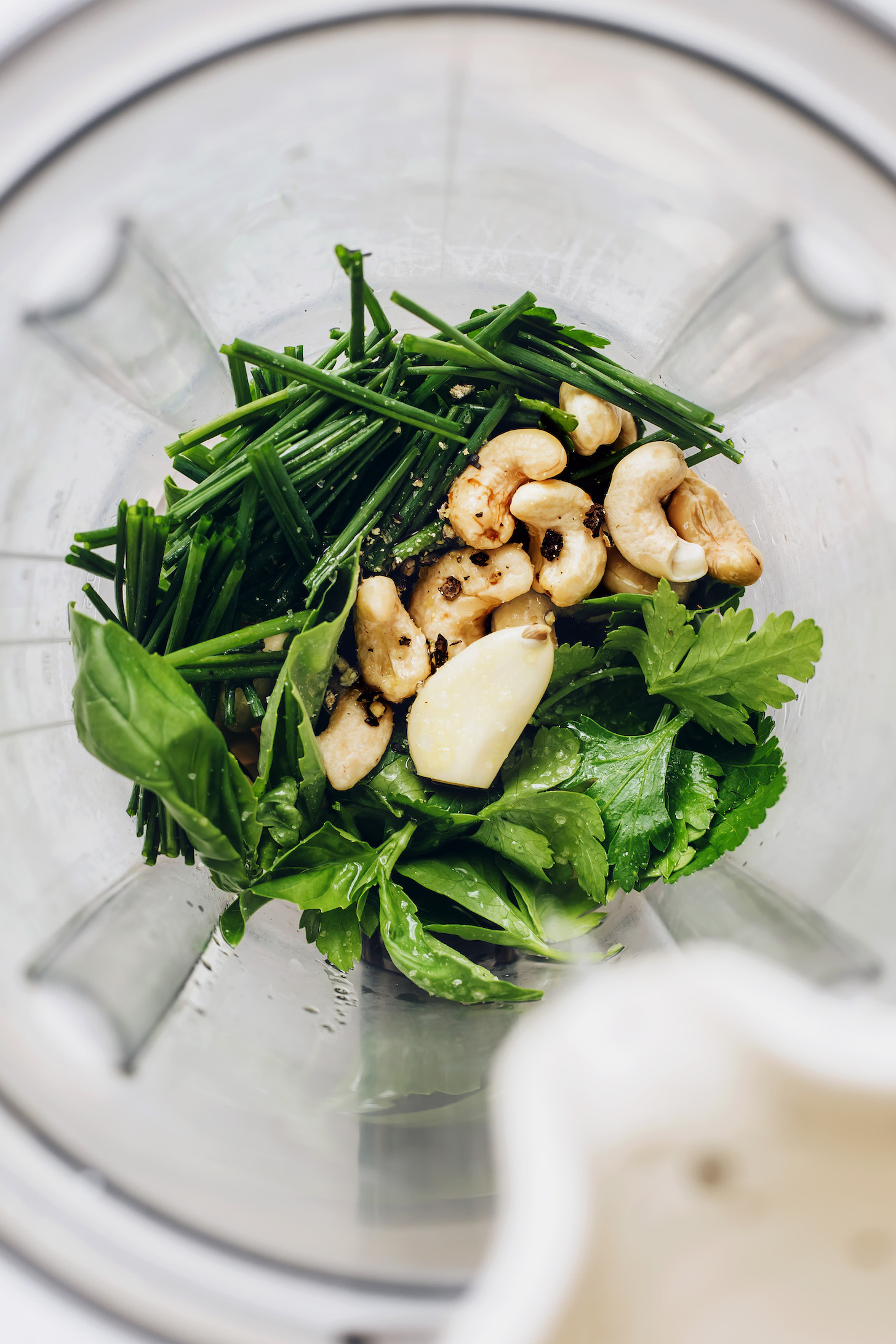 Blender with fresh herbs, cashews, garlic, and black pepper