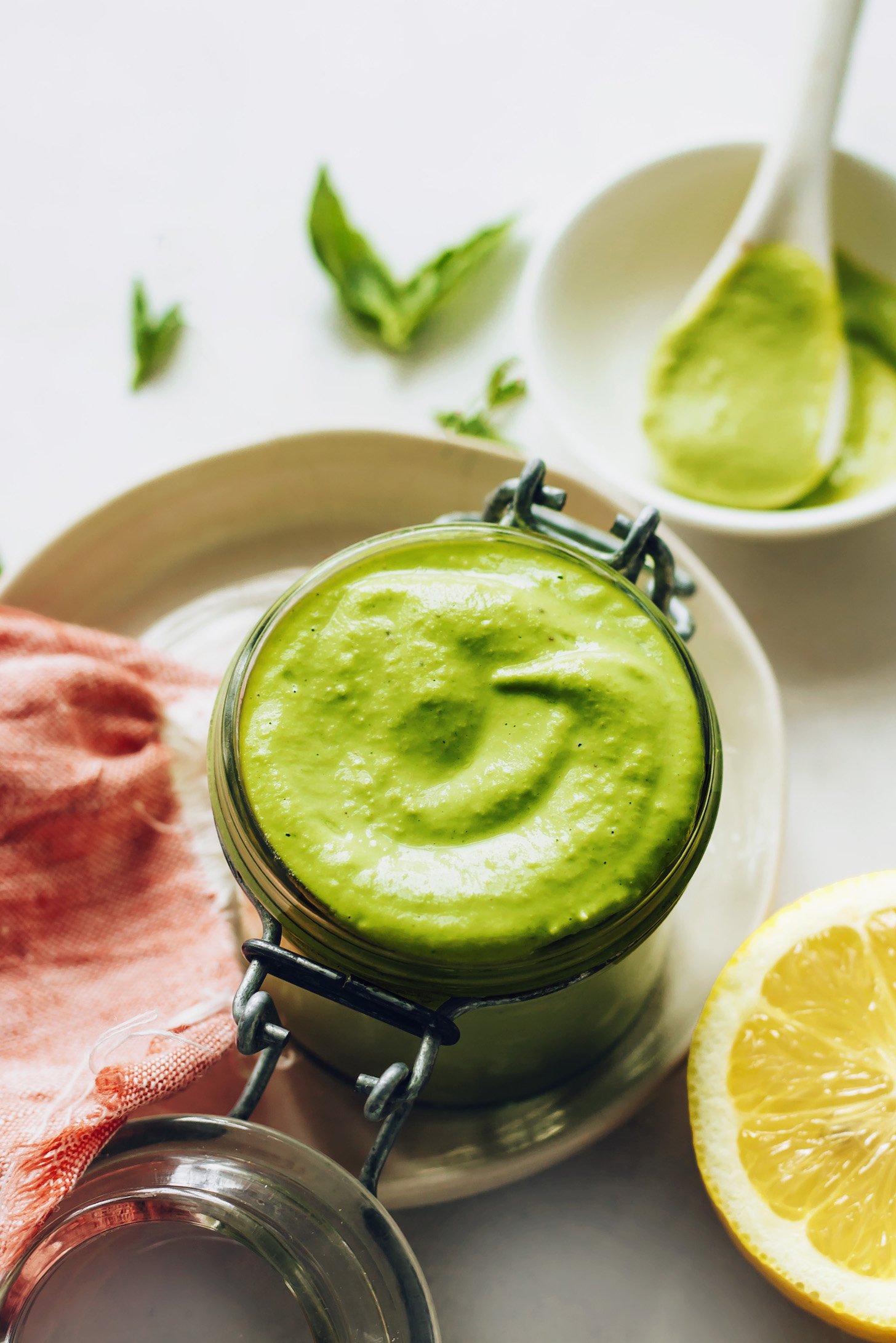 Jar of green goddess dressing next to a halved lemon and fresh herbs