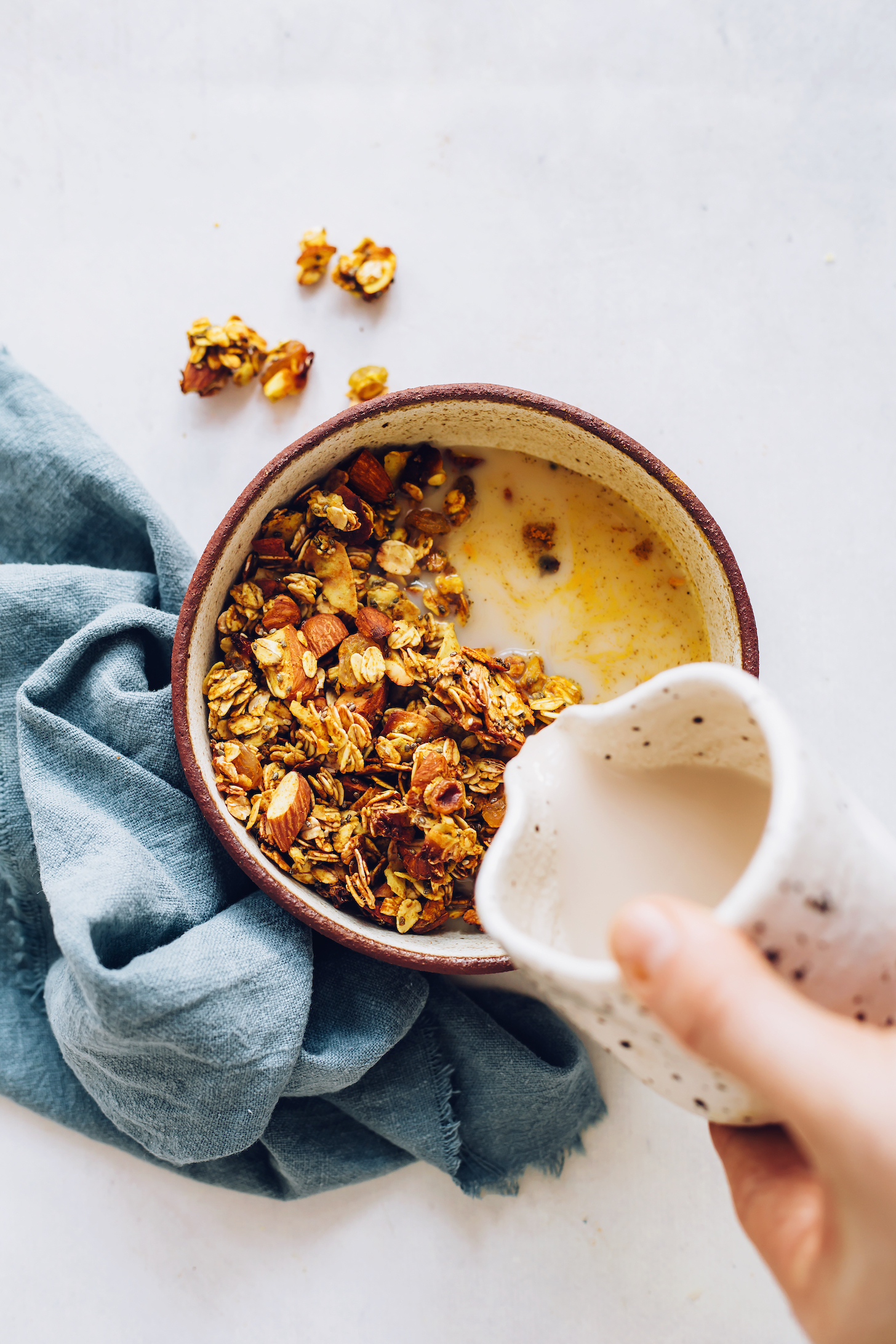 Pouring dairy-free milk into a bowl of golden milk granola