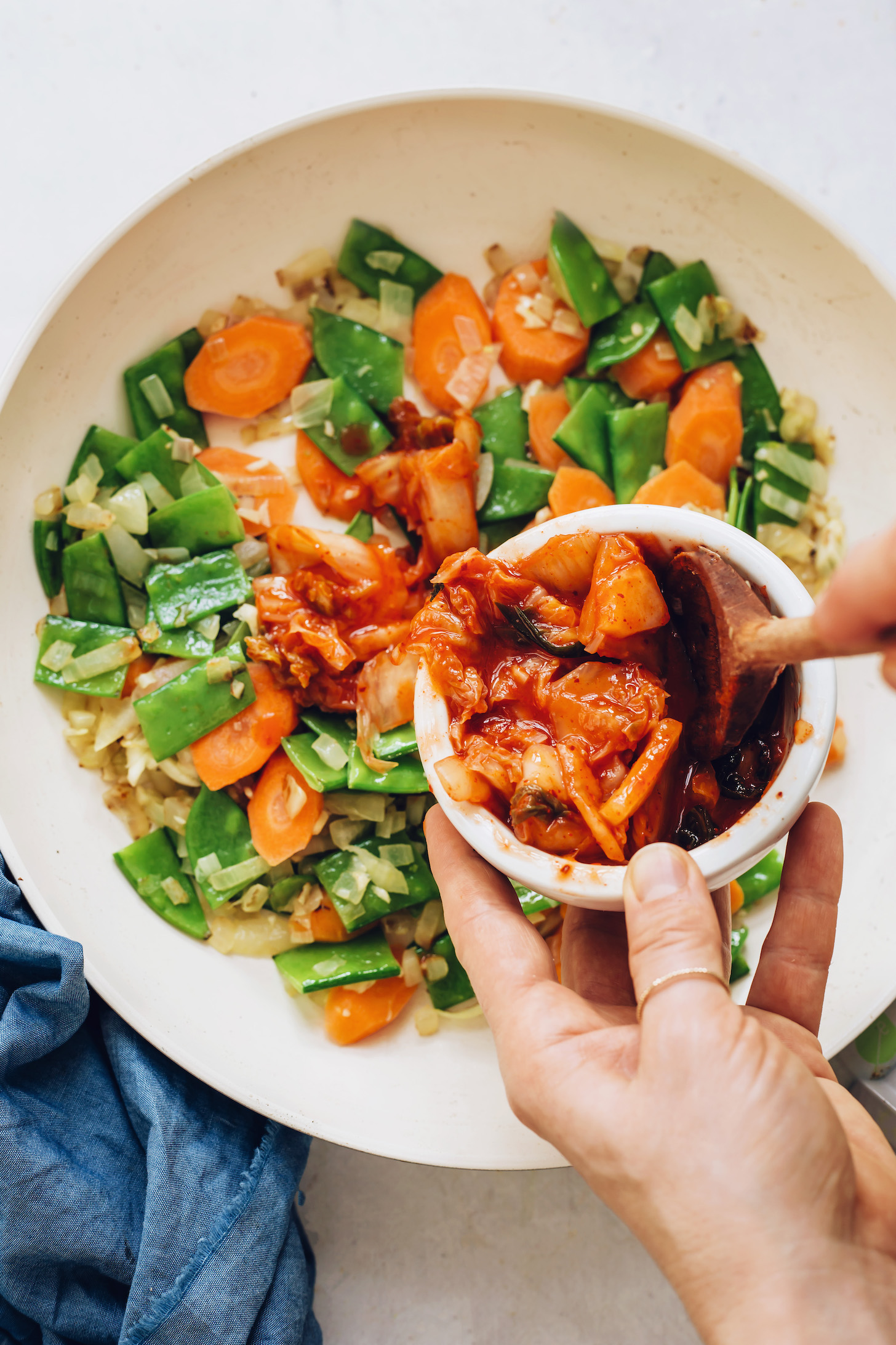 Adding kimchi to a pan of sautéed vegetables