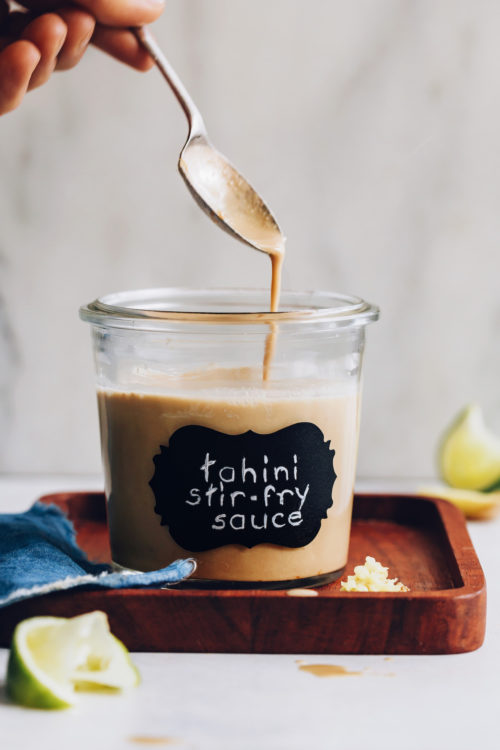 Tahini stir fry sauce dripping from a spoon into a jar