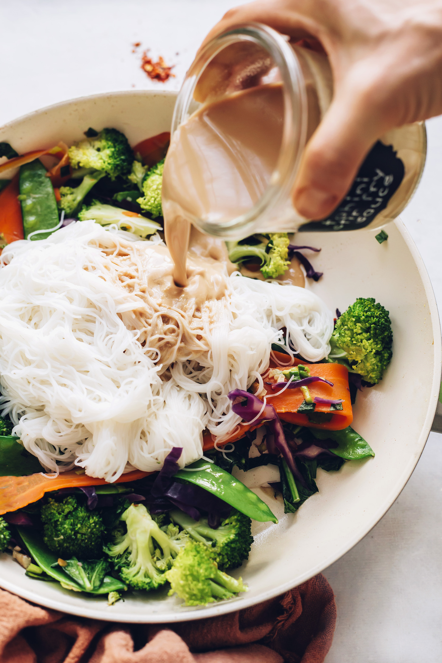 Pouring tahini stir fry sauce over noodles and veggies