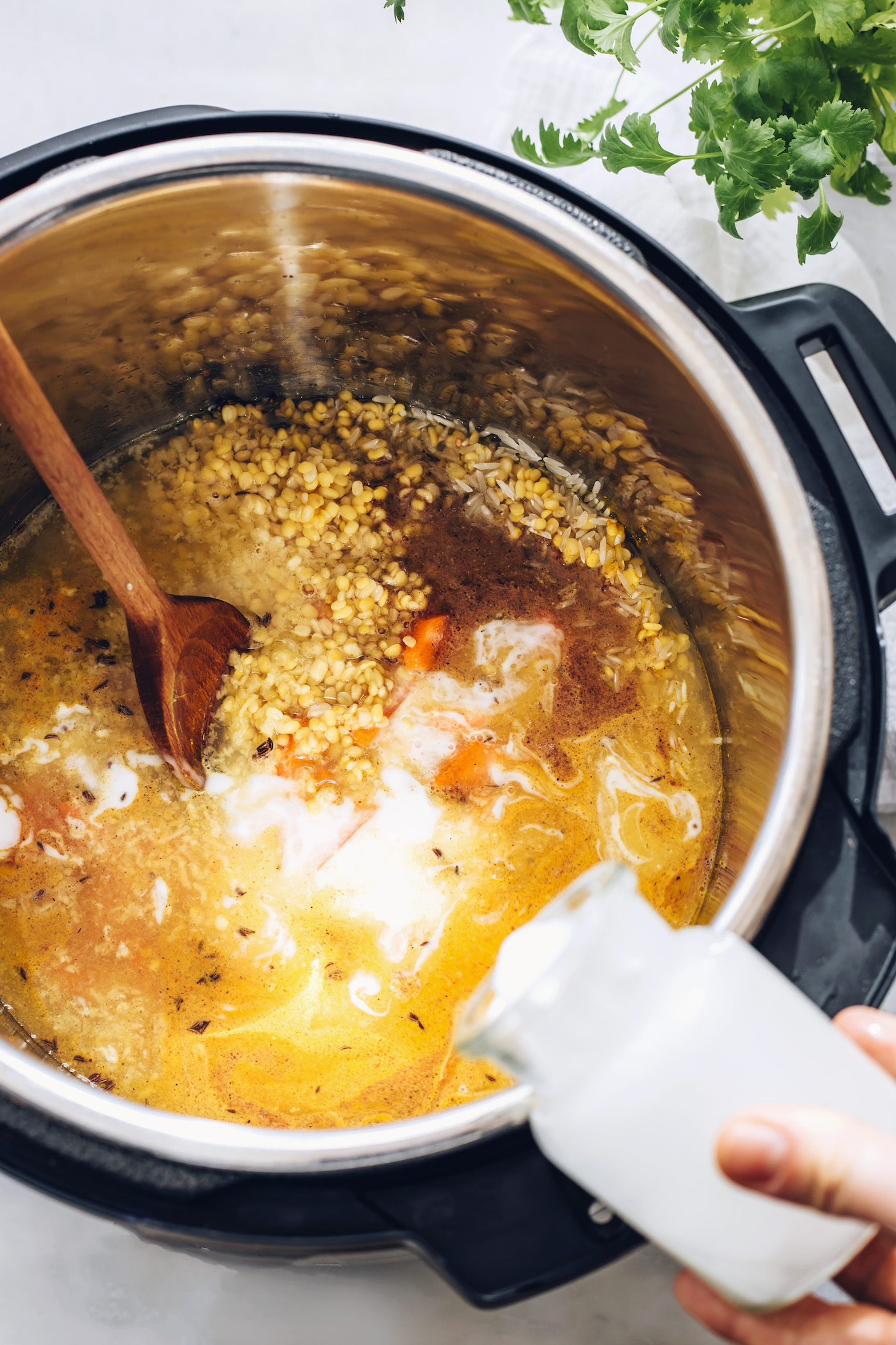 Pouring coconut milk into a pot of kitchari