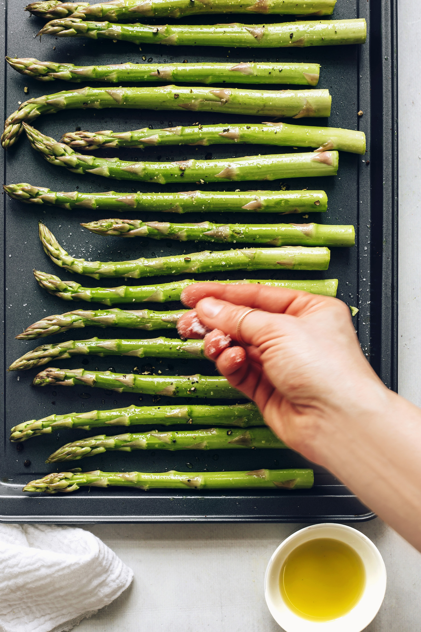 Sprinkling sea salt and black pepper over a pan of asparagus