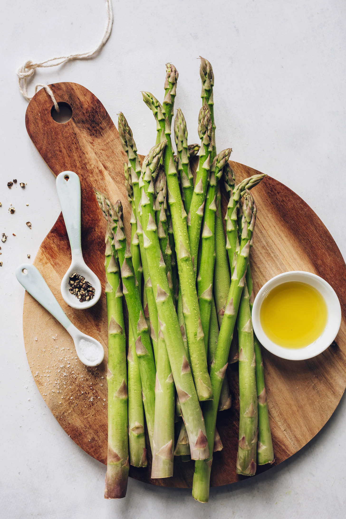 Cutting board of asparagus spears, olive oil, salt, and pepper