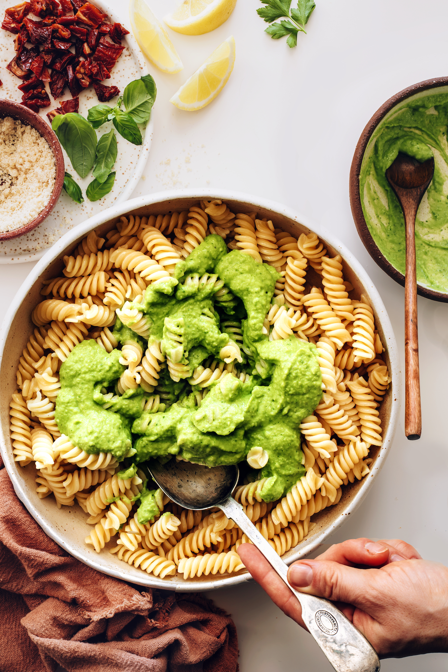 Using a vintage spoon to stir avocado herb pesto on gluten-free noodles