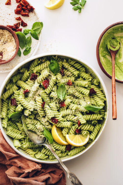 Large plate of creamy avocado pesto pasta salad next to a bowl of avocado pesto