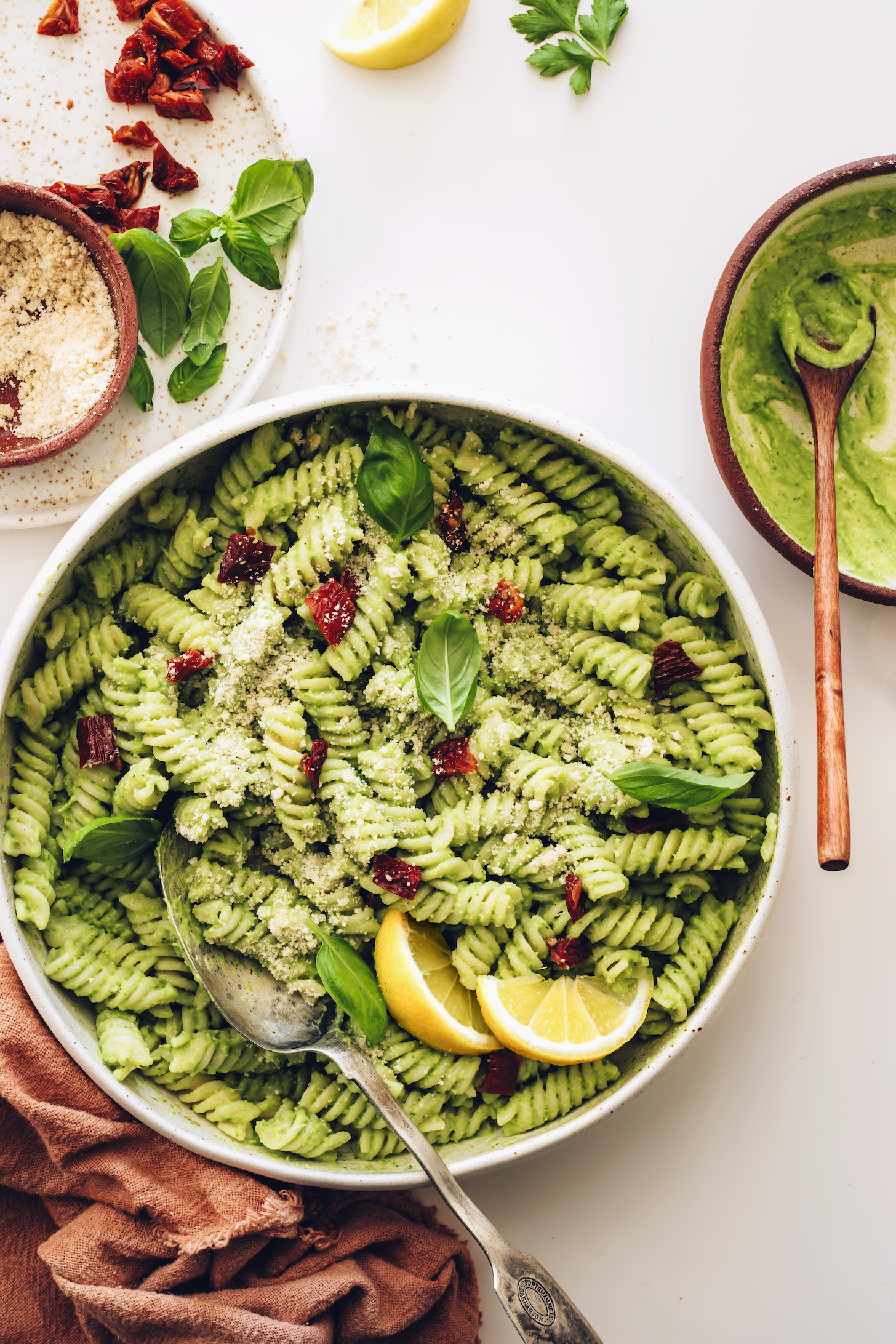 Large platter of avocado pesto pasta with fresh basil, sun-dried tomatoes, and vegan parmesan cheese