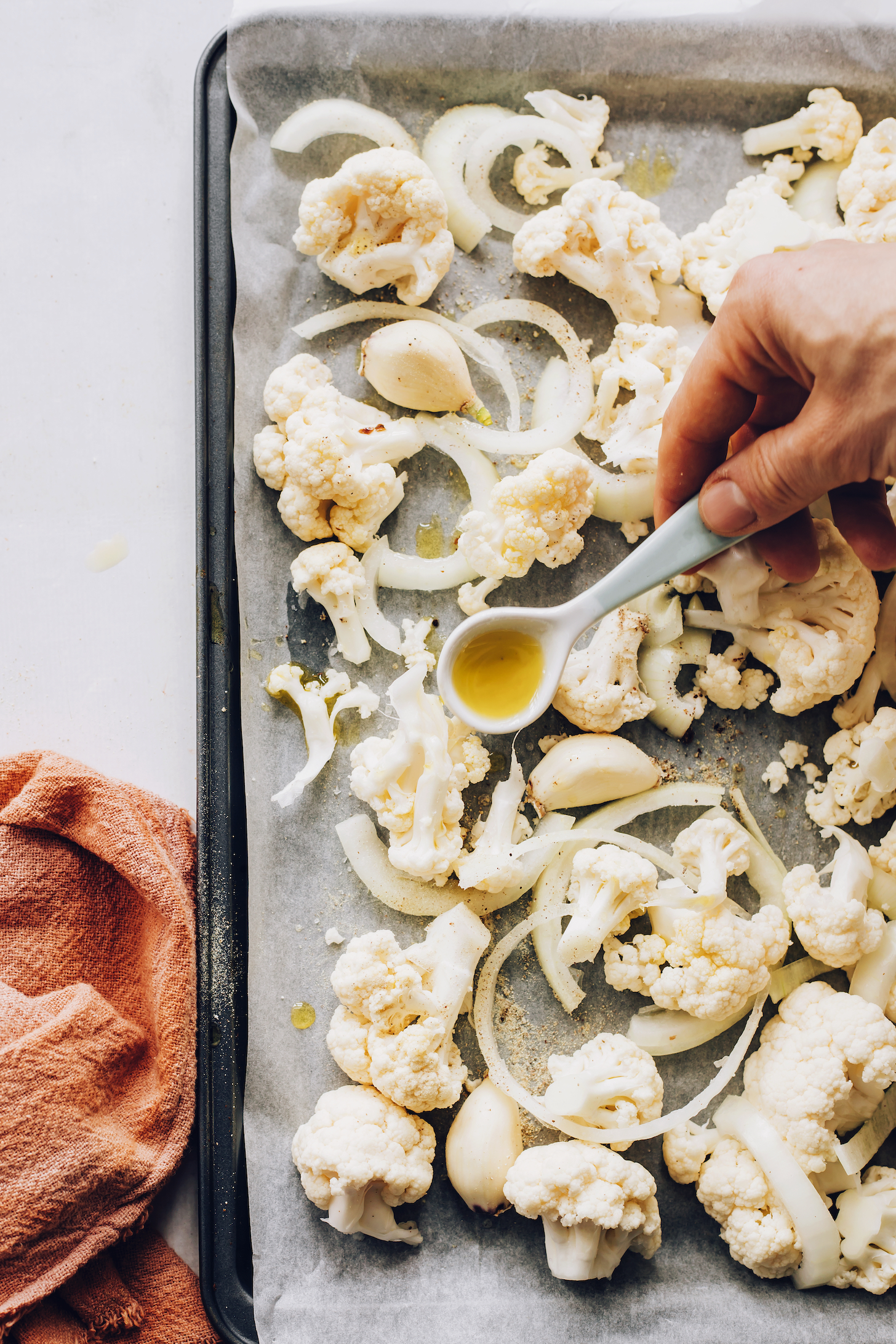 Pouring avocado oil over a baking sheet of cauliflower and onions