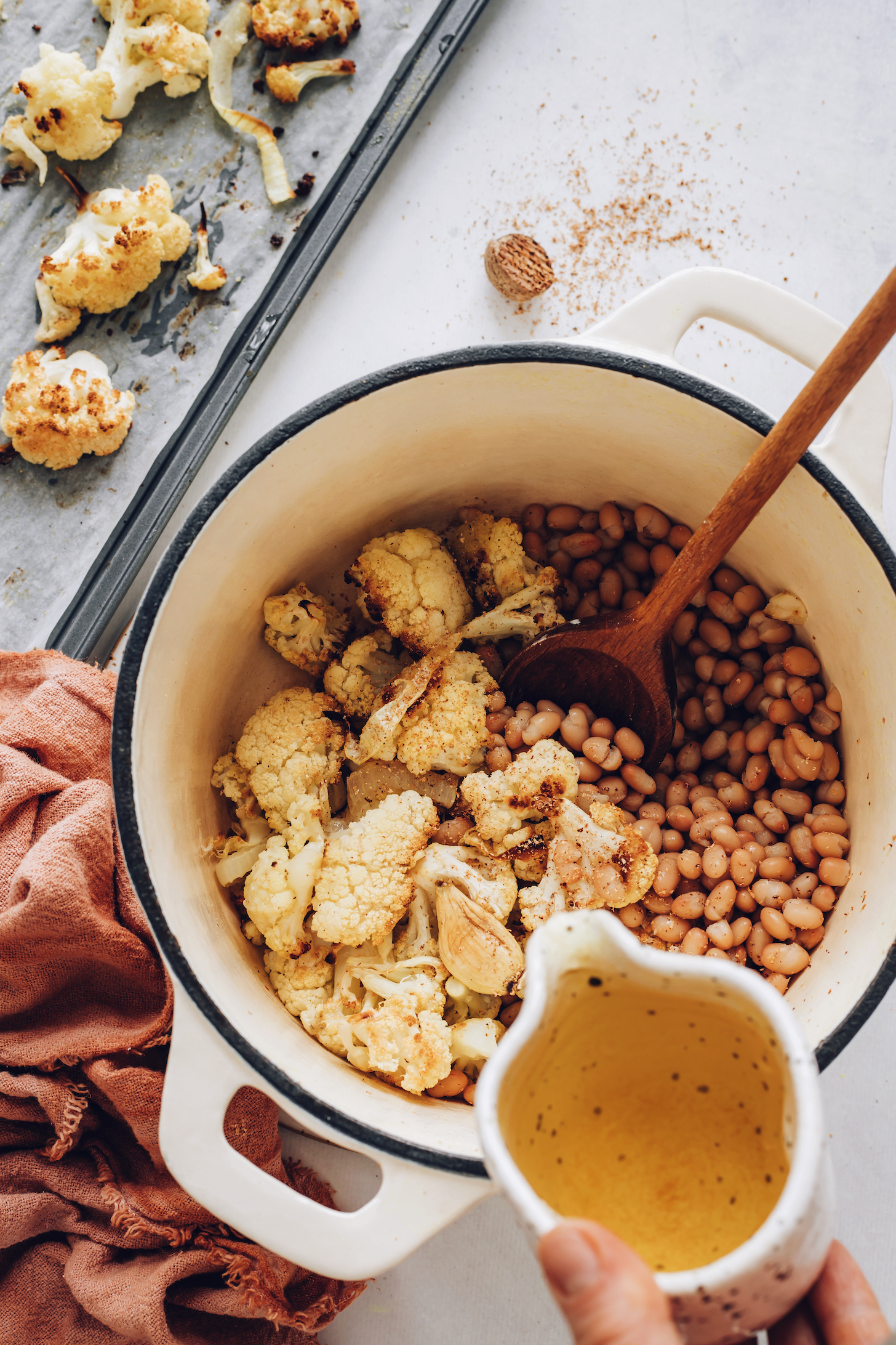 Pouring vegetable broth into a pot of roasted cauliflower soup