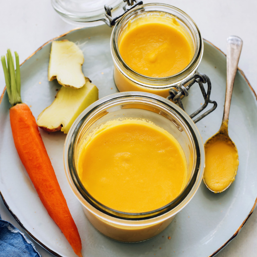 Two jars of carrot ginger dressing next to fresh ginger and a carrot
