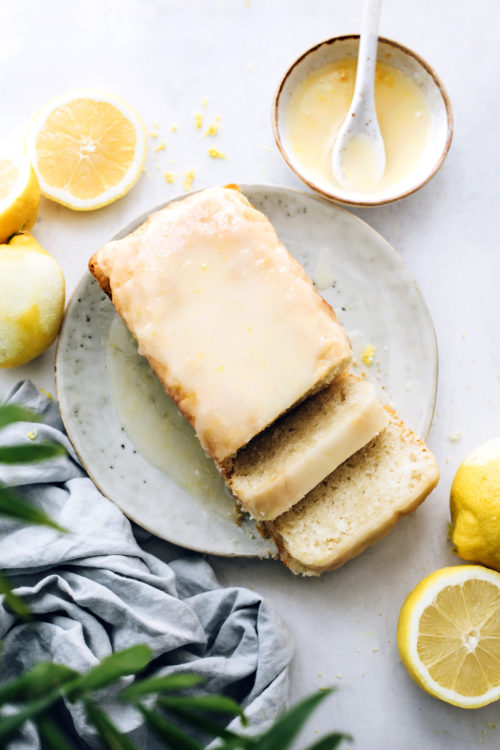Sliced lemon loaf cake next to a bowl of lemon glaze