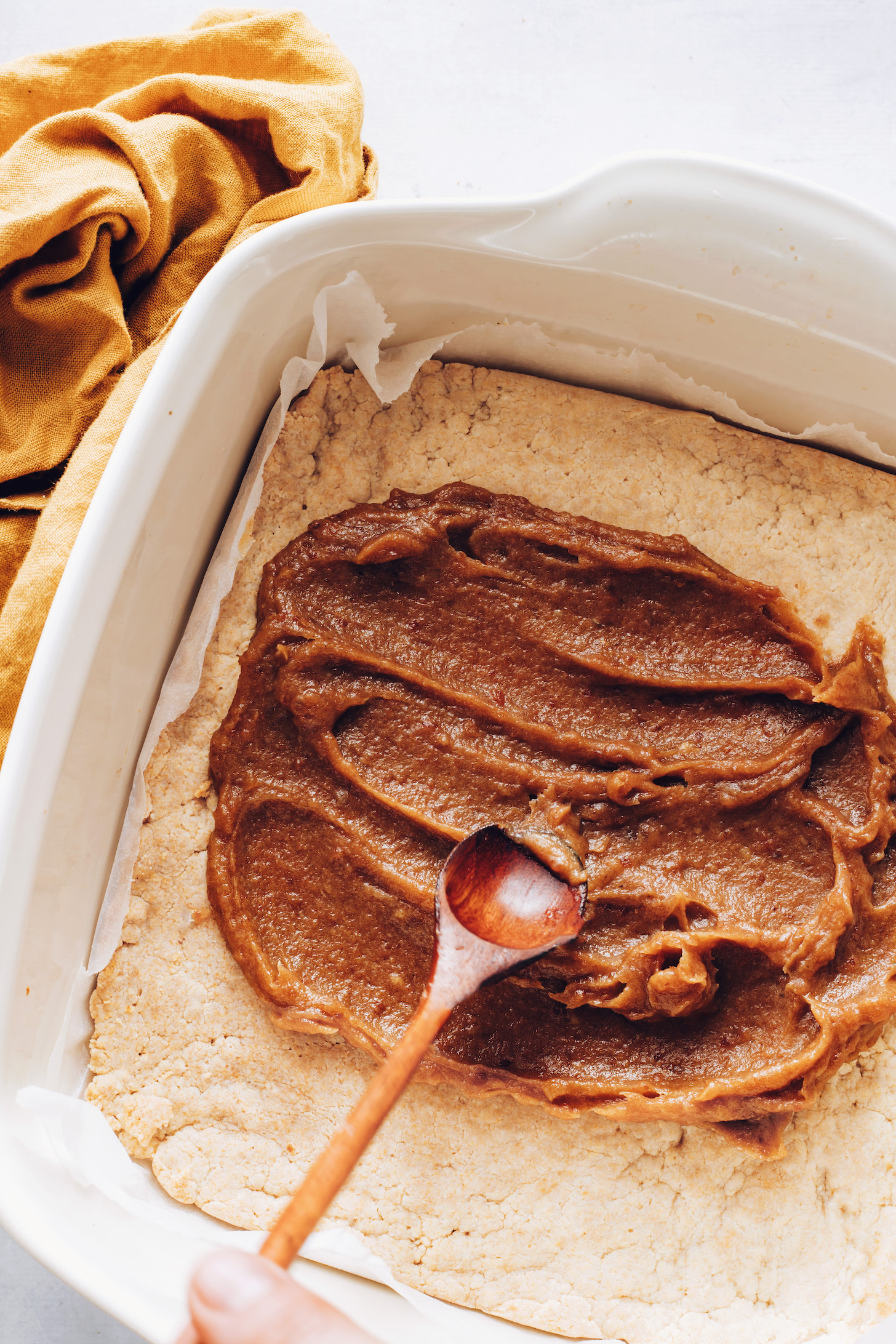 Spreading date caramel onto a crunchy cookie layer in a baking dish