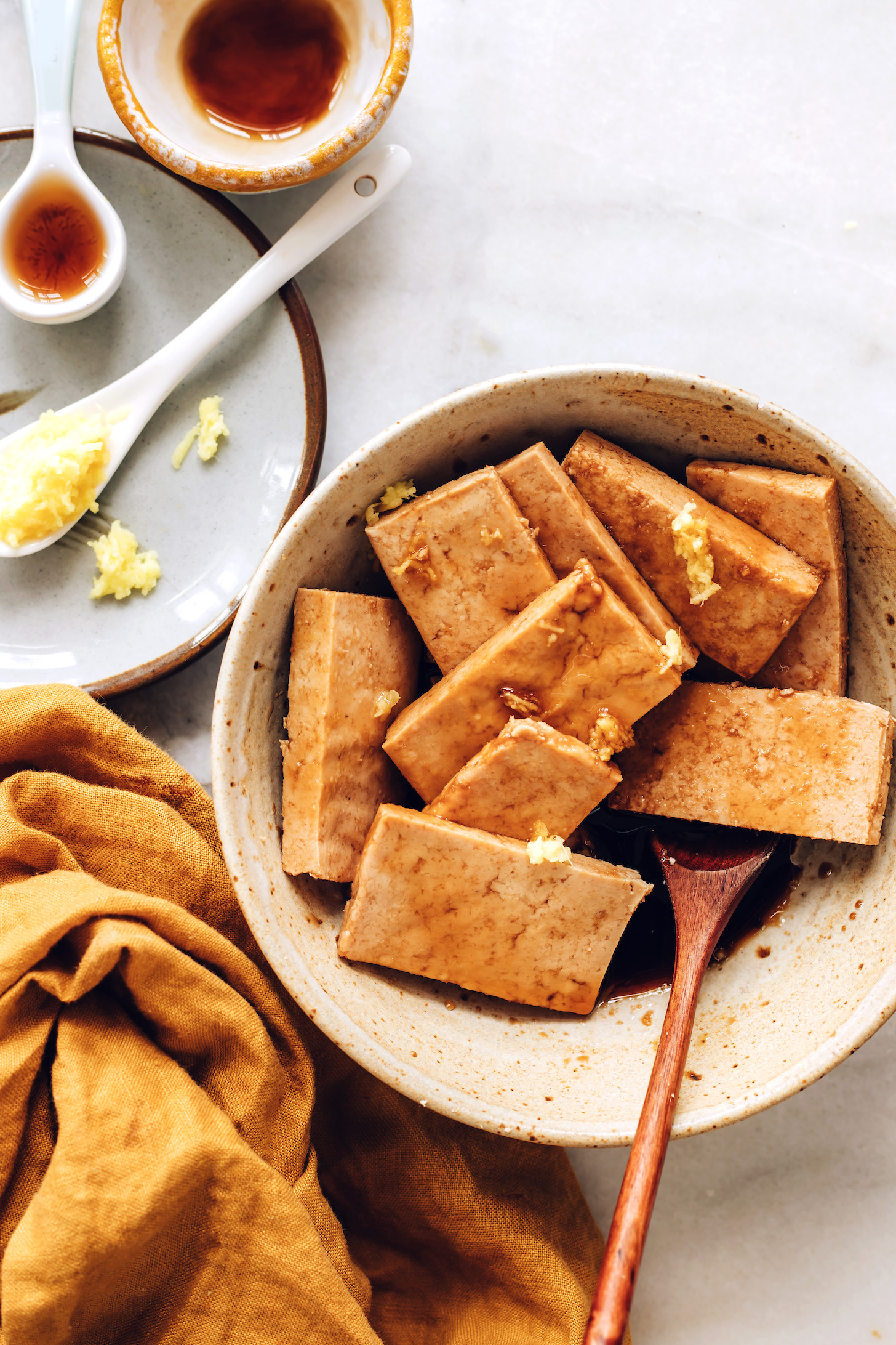 Ginger, maple syrup, and sesame oil next to a bowl of ginger marinated tofu
