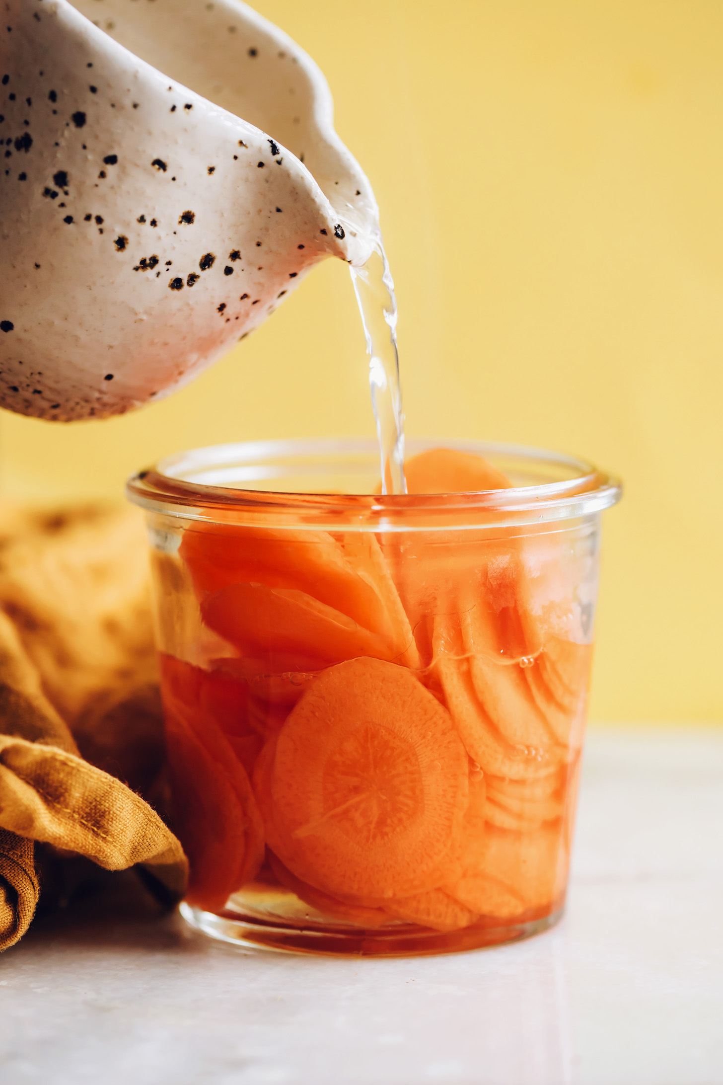 Pouring a vinegar and water mixture over thinly sliced carrots