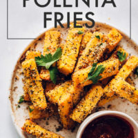 Plate of polenta fries with one dipped in a bowl of marinara