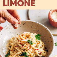 Sprinkling red pepper flakes onto a bowl of vegan lemon pasta