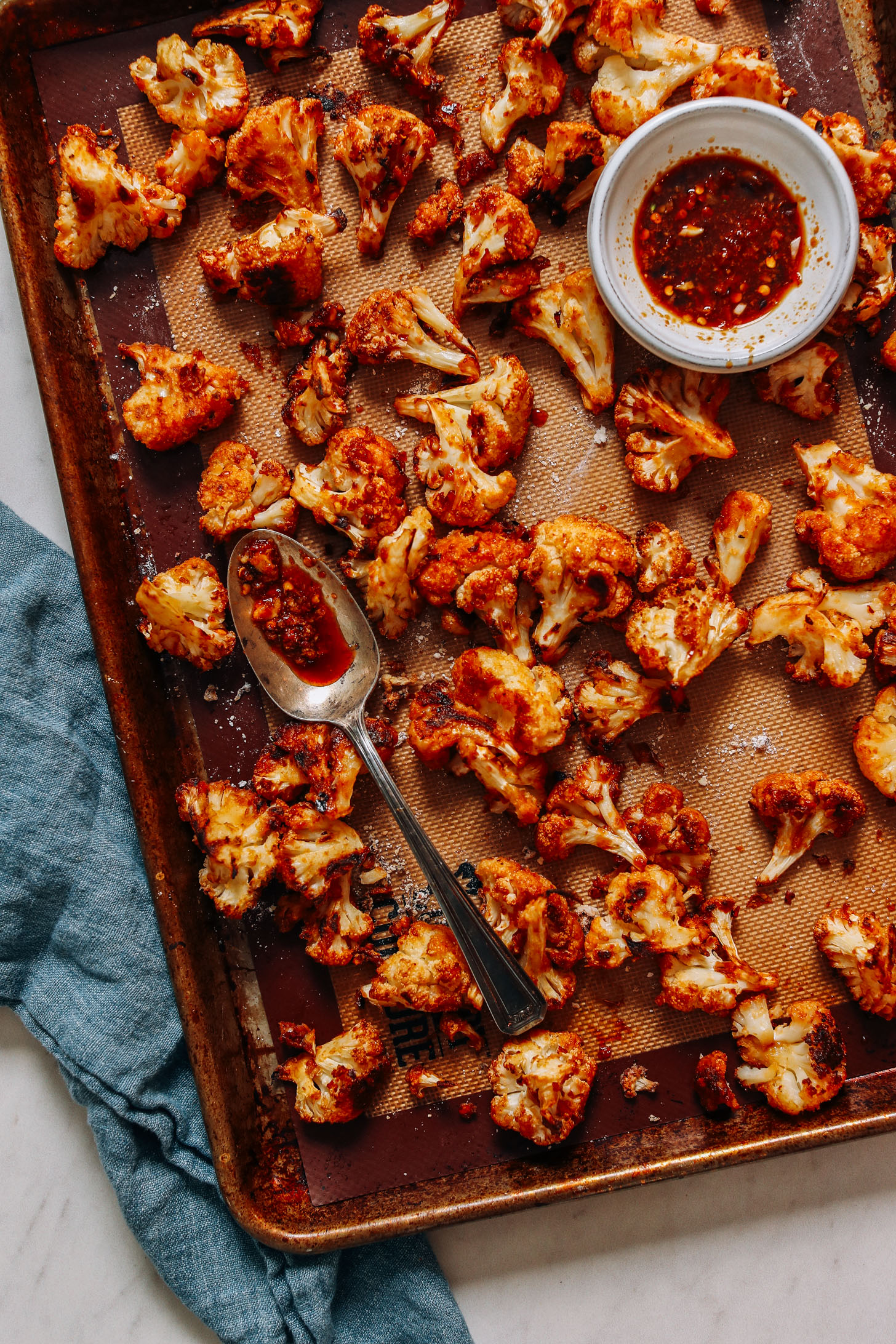 Baking sheet of General Tsos's Cauliflower with a bowl of chili garlic sauce