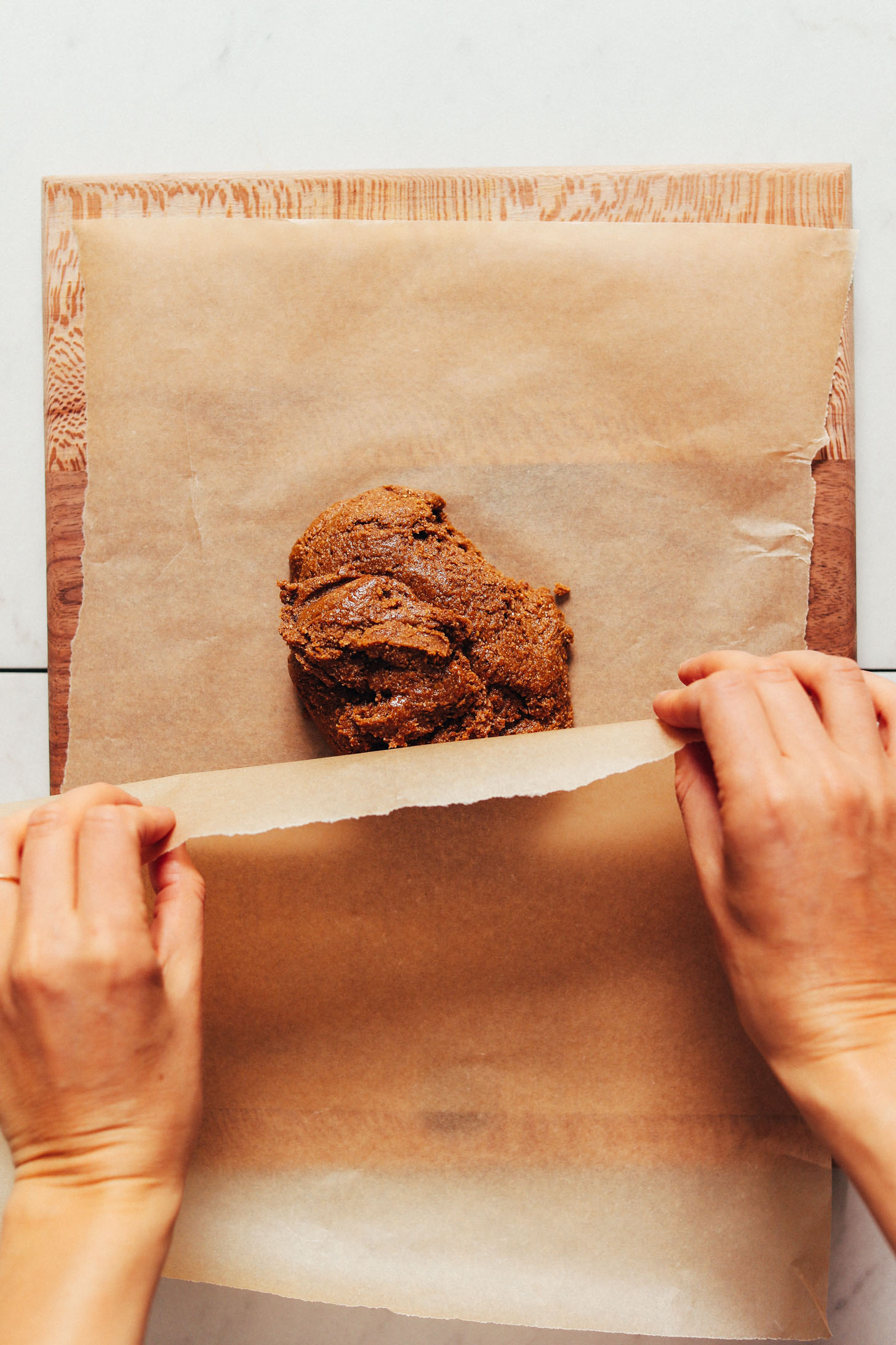 Placing parchment paper over a ball of gluten-free graham cracker dough to roll it flat