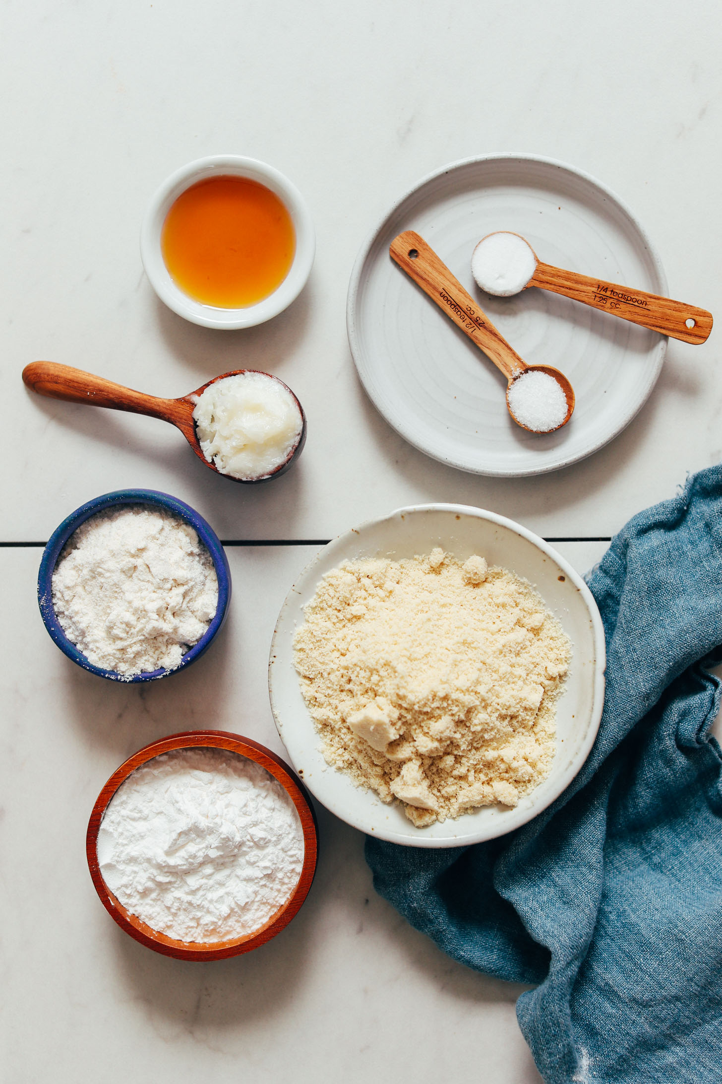 Bowls and spoonfuls of almond flour, gluten-free flour blend, tapioca flour, baking soda, sea salt, coconut oil, and maple syrup