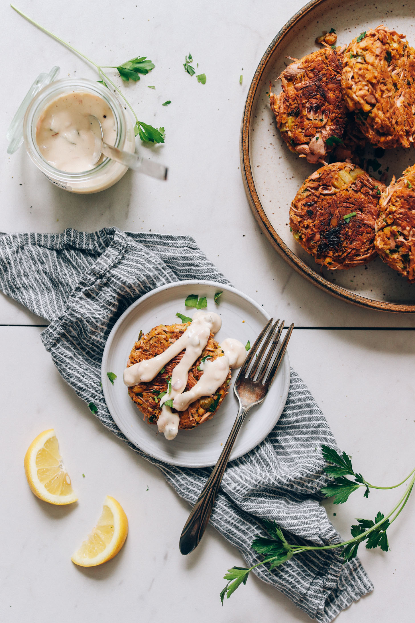 Vegan tartar sauce drizzled over a vegan crab cake next to a larger plate of crab cakes