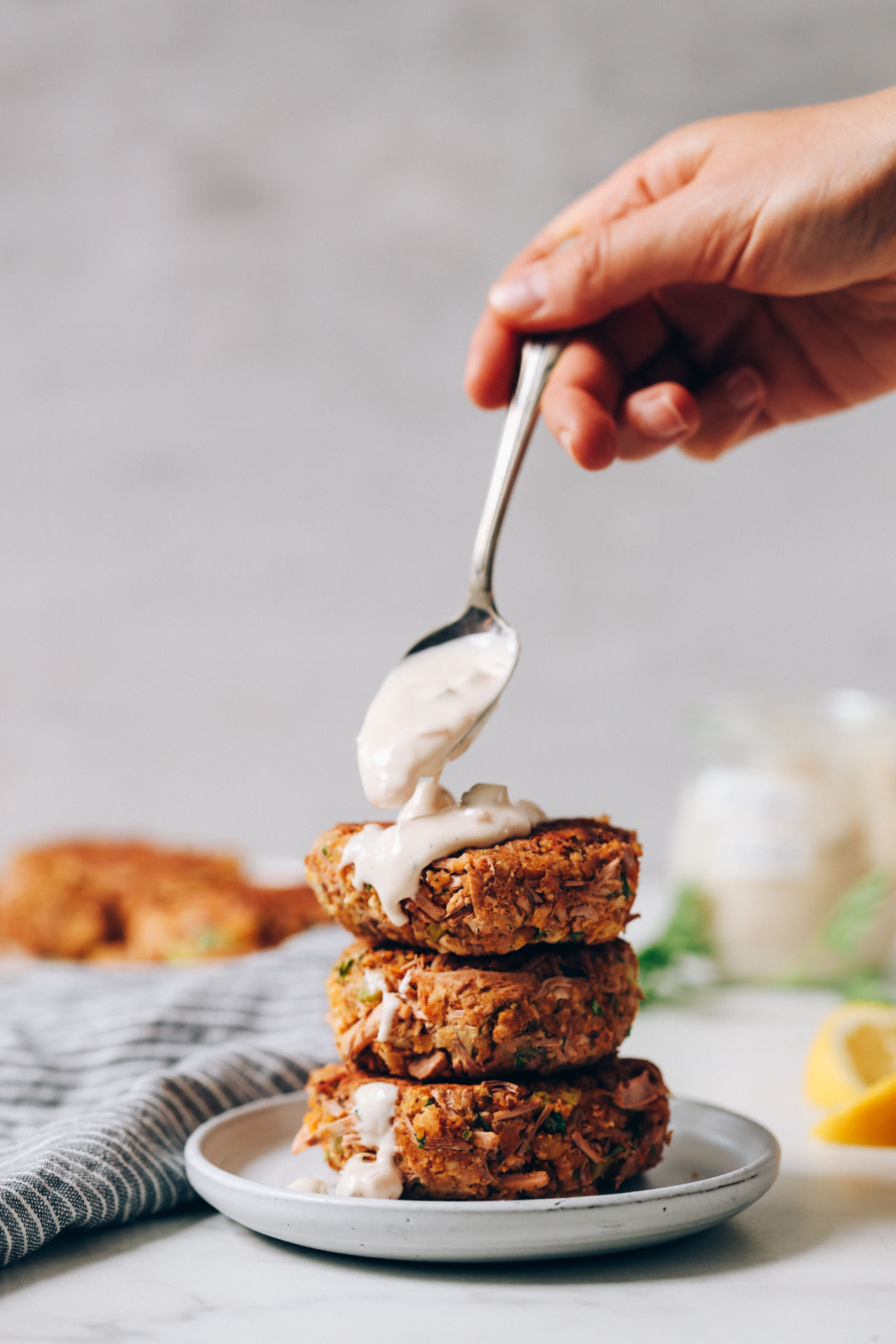 Drizzling vegan tartar sauce over a stack of vegan crab cakes