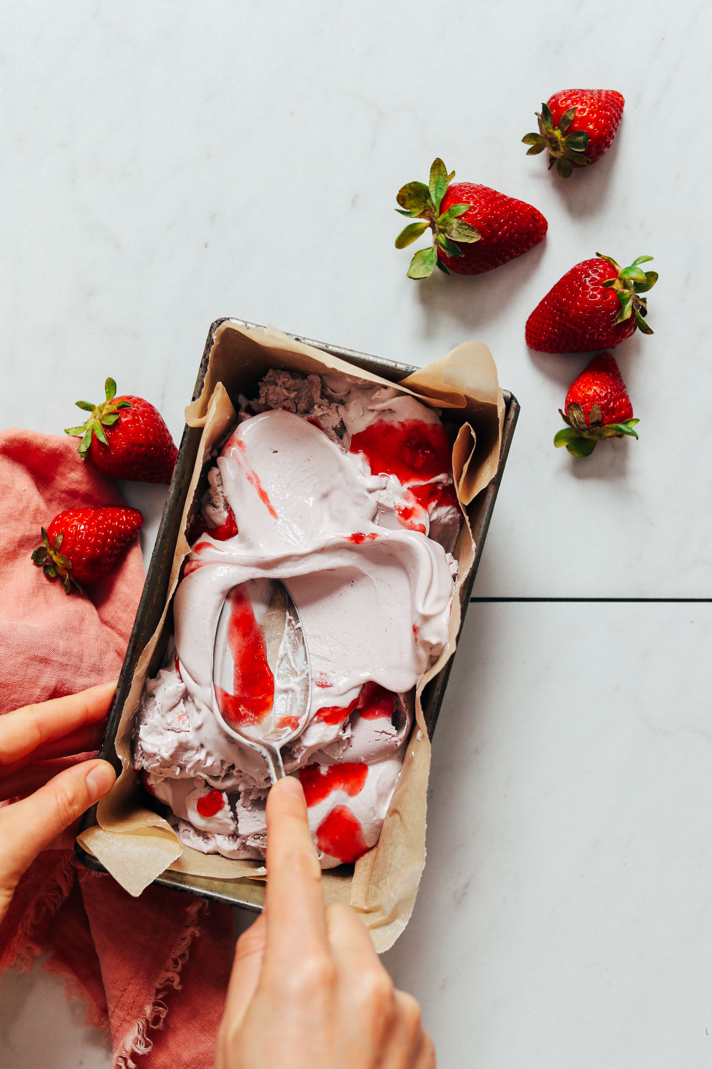 Adding strawberry compote swirls to a pan of vegan strawberry ice cream