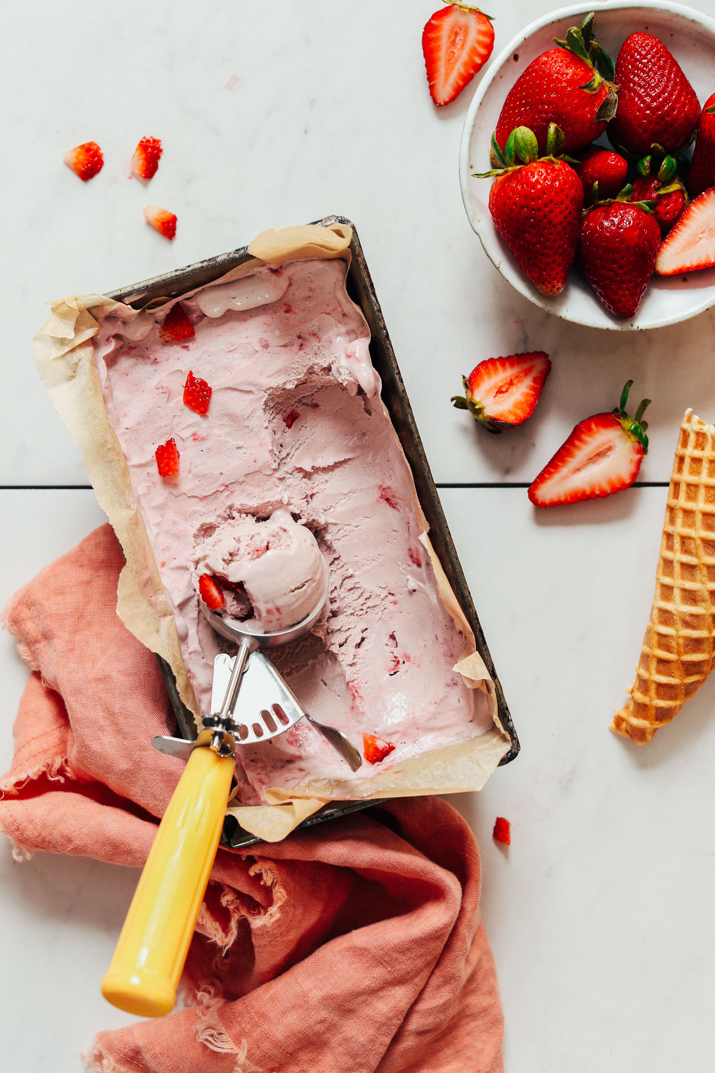 Ice cream scoop in a loaf pan of vegan strawberry ice cream