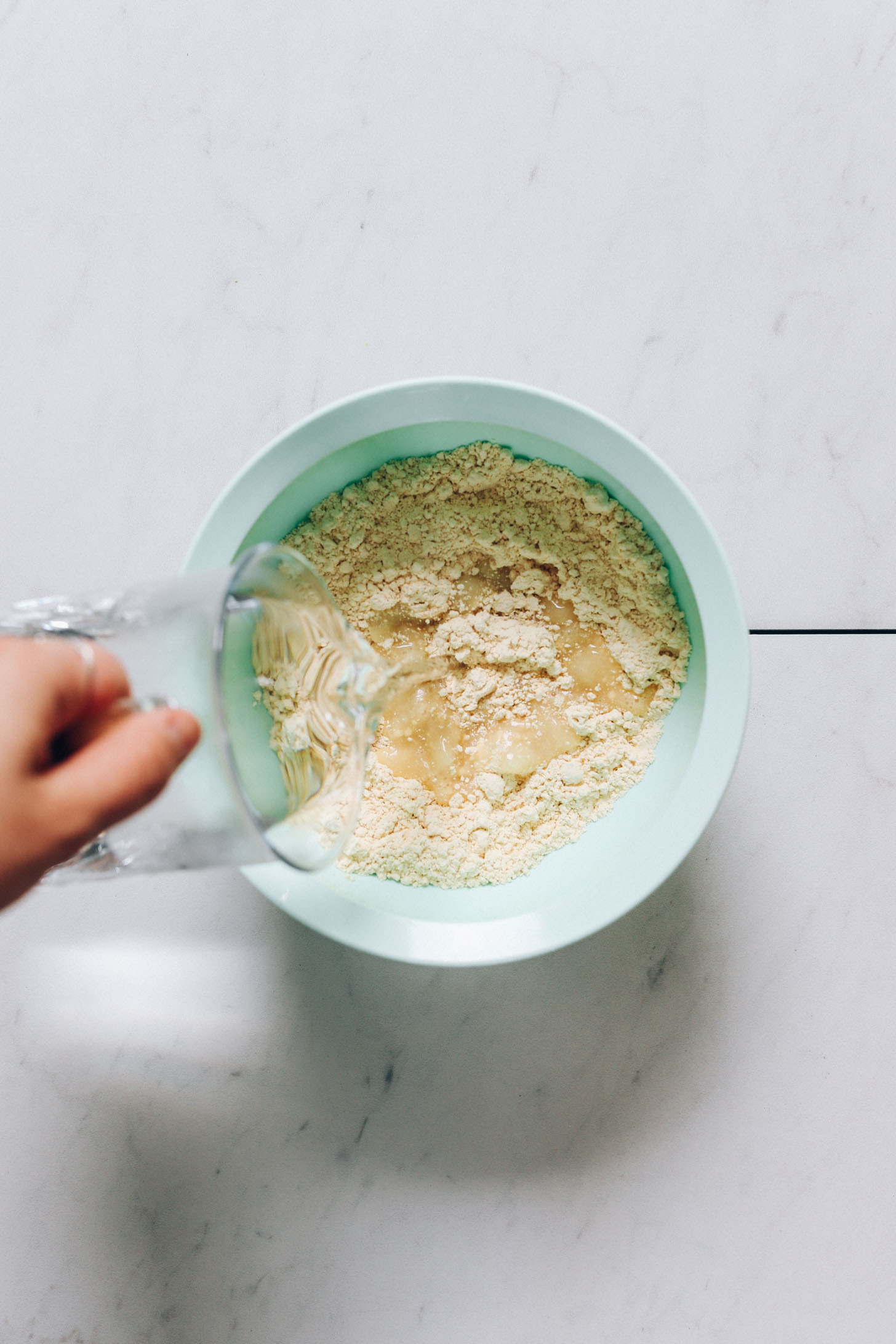 Pouring water into a bowl of chickpea flour and salt