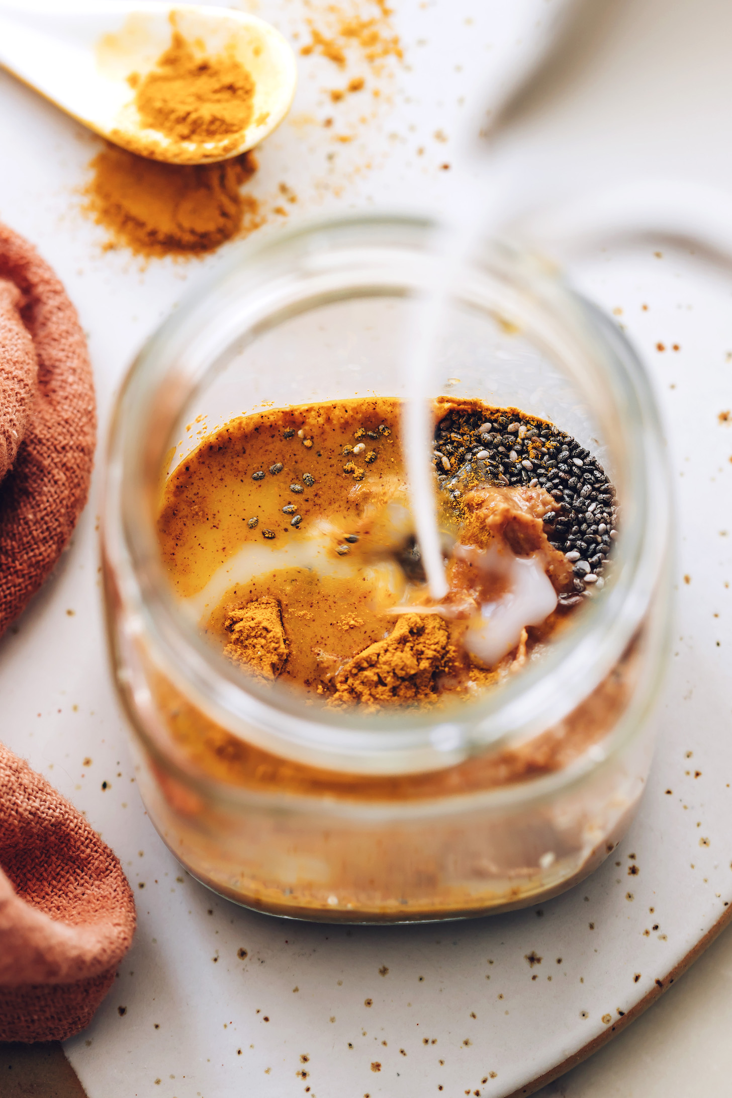 Pouring coconut milk into a jar to make golden milk overnight oats
