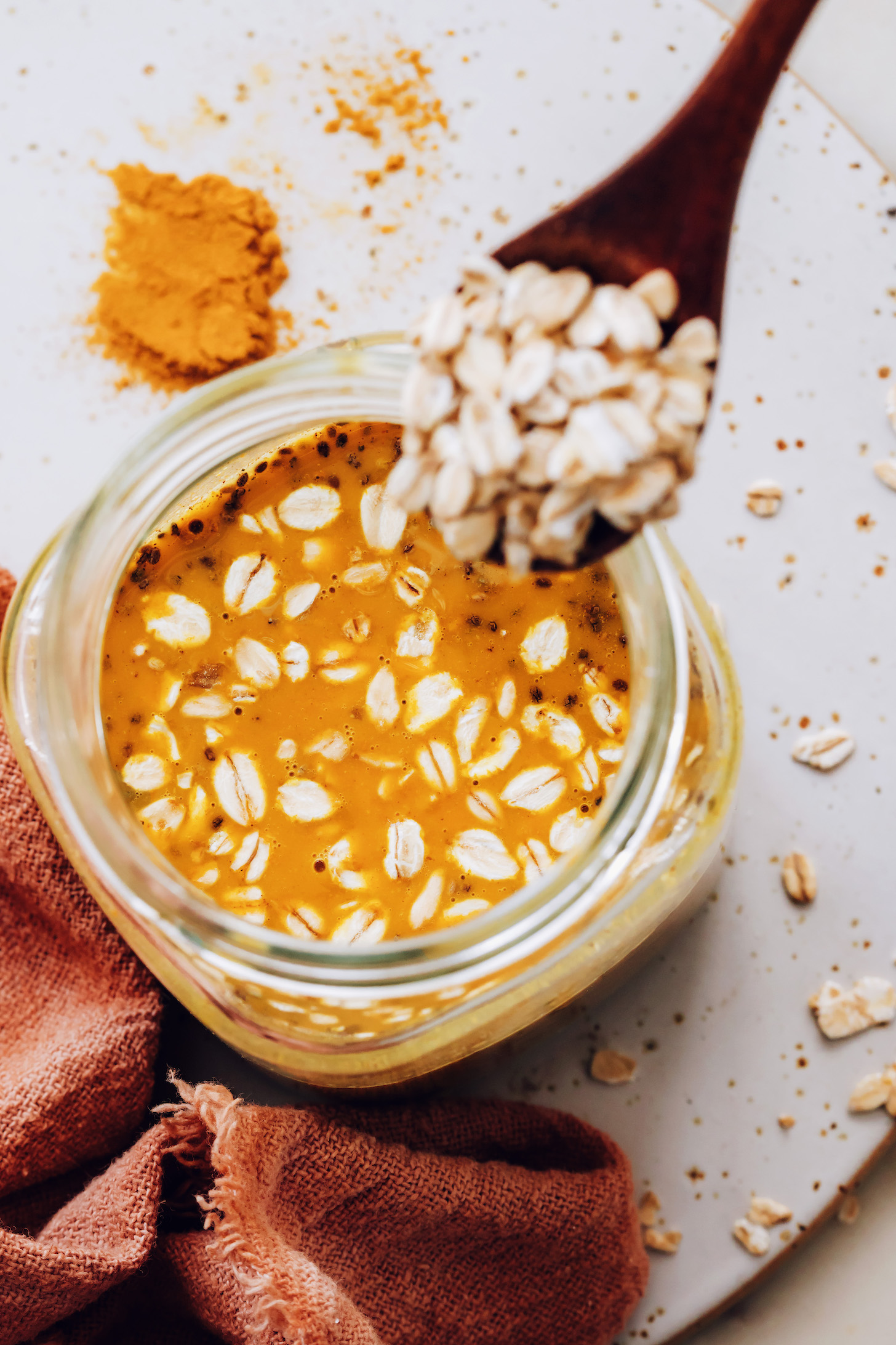 Pouring rolled oats into a jar with coconut milk and other ingredients for golden milk overnight oats