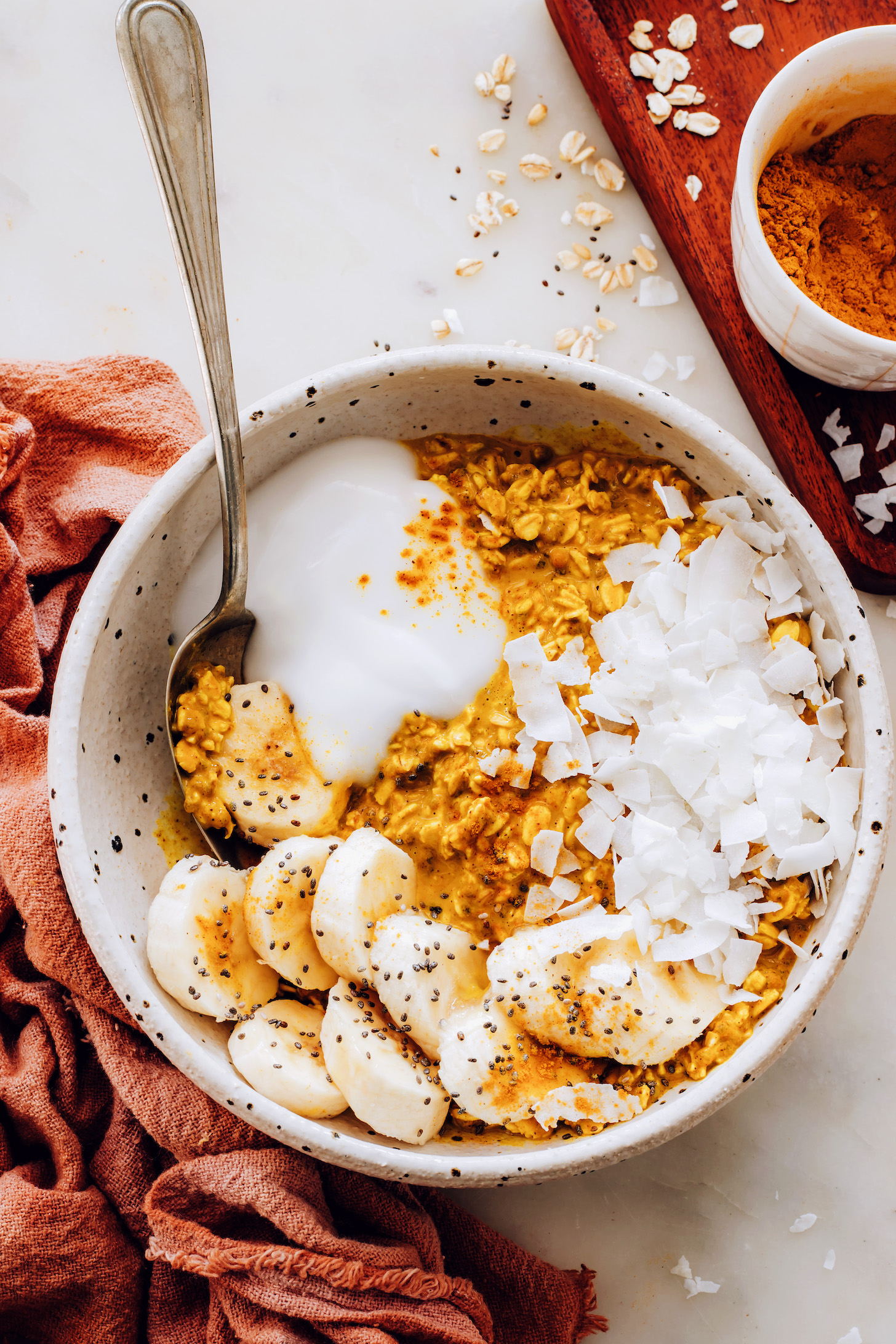 Bowl of golden milk overnight oats with coconut flakes, chia seeds, and banana