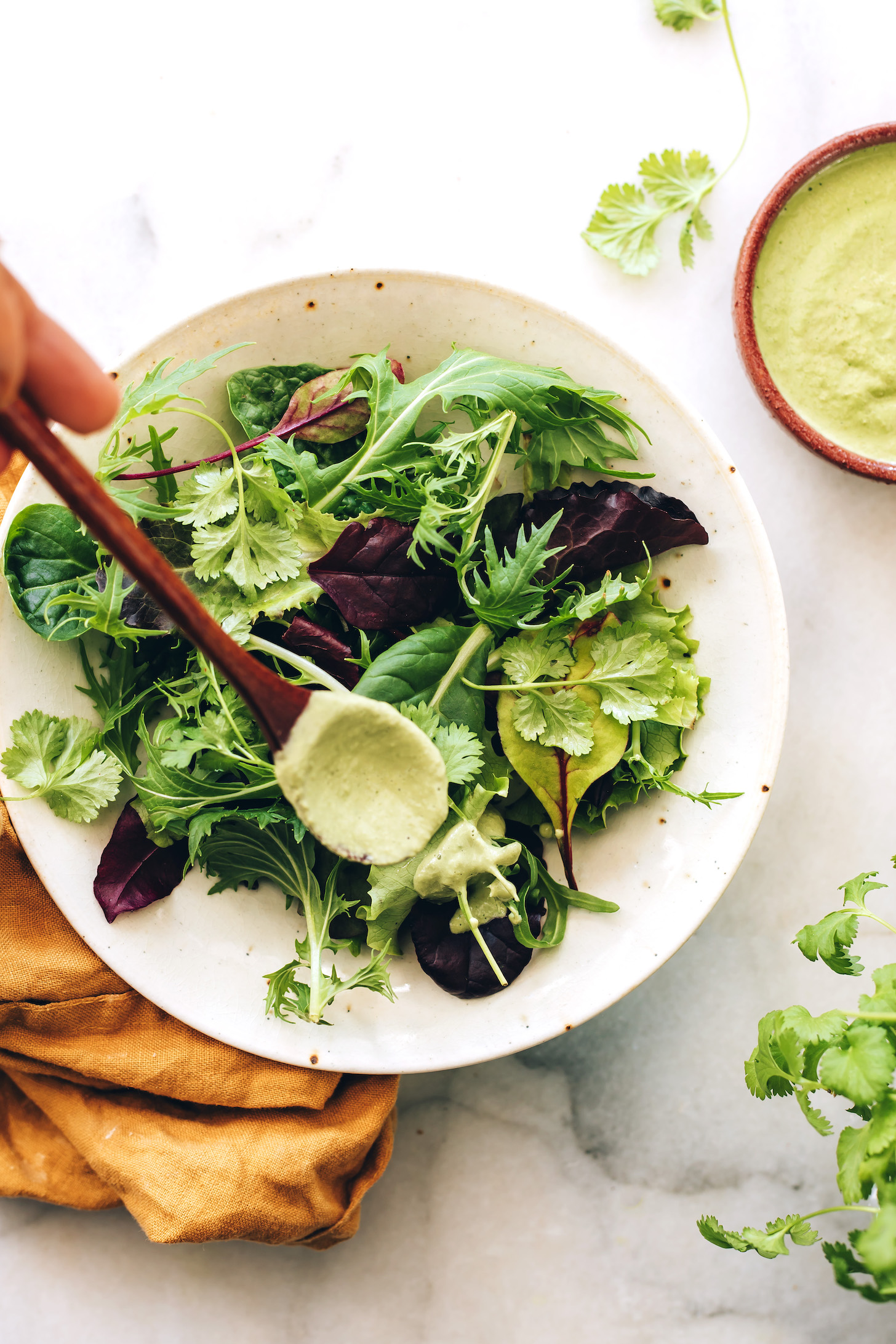 Drizzling cilantro sunflower seed dressing over a bowl of greens