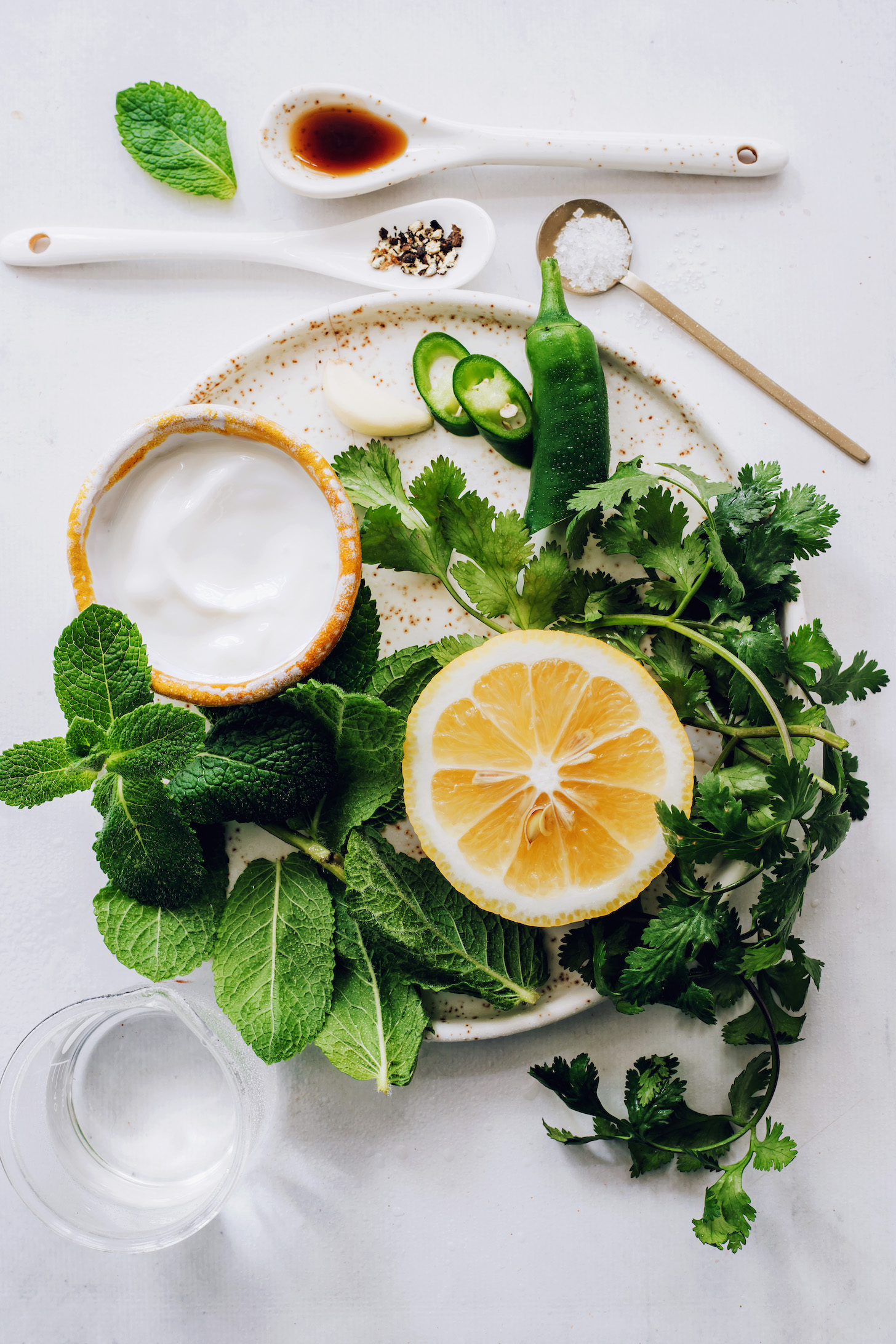 Maple syrup, salt, pepper, and water around a plate with coconut yogurt, mint, cilantro, lemon, jalapeno, and garlic