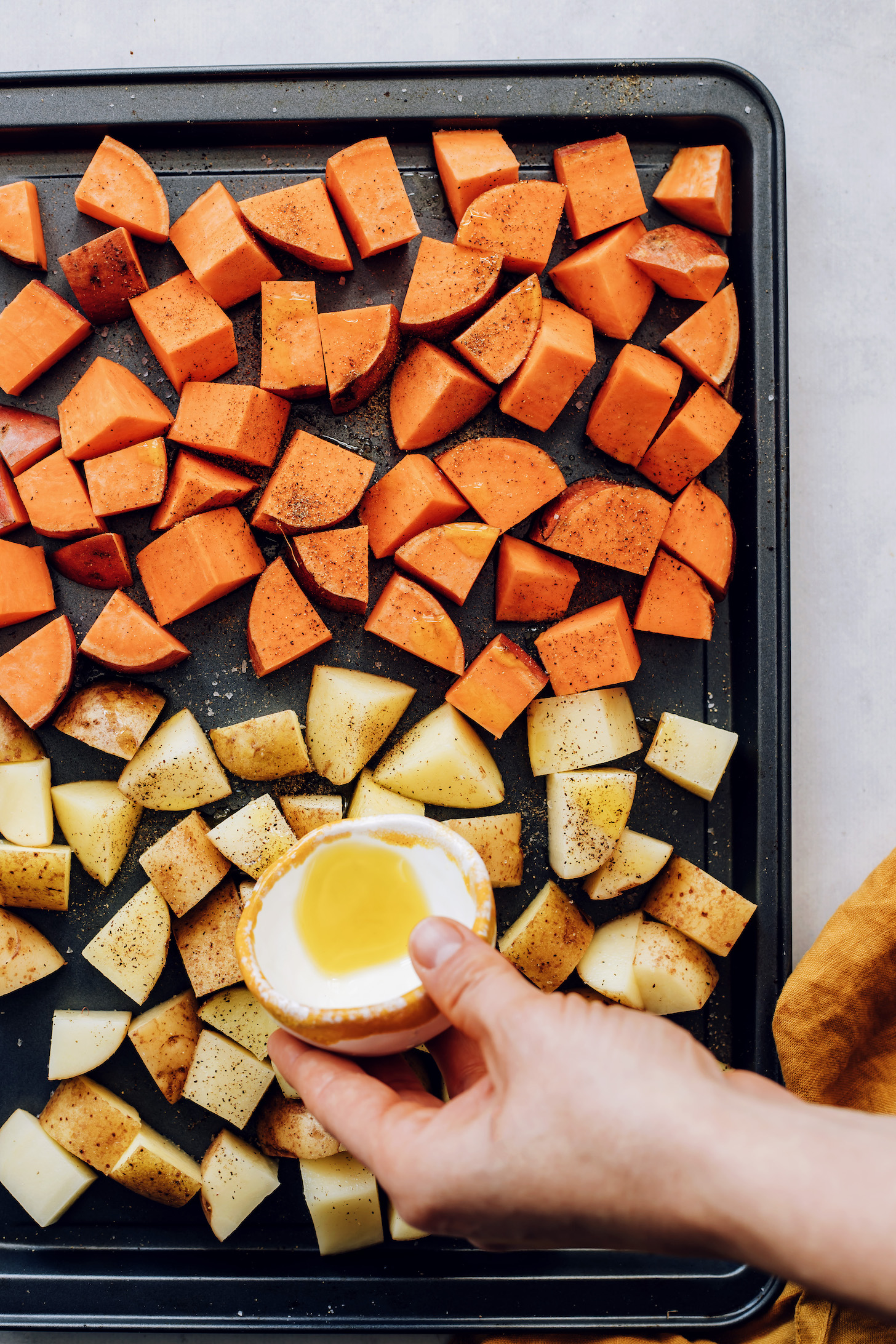 Drizzling avocado oil over sliced gold and sweet potatoes