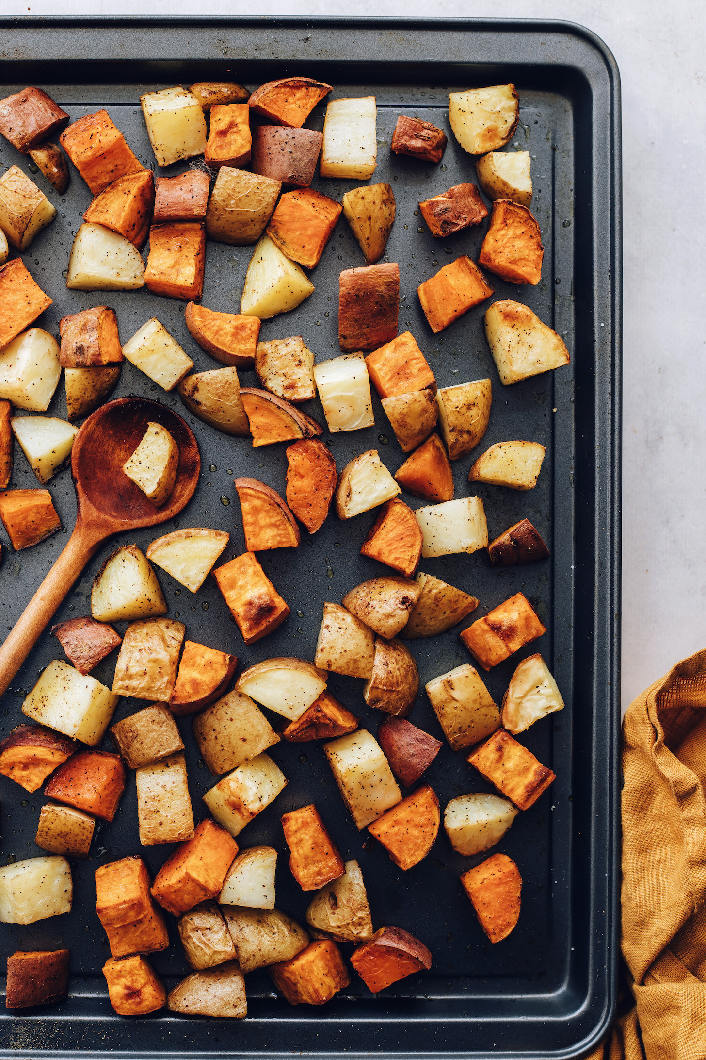 Wooden spoon on a baking sheet of roasted gold and sweet potatoes