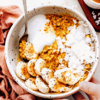 Bowl of golden milk overnight oats topped with banana, coconut yogurt, coconut flakes, and chia seeds